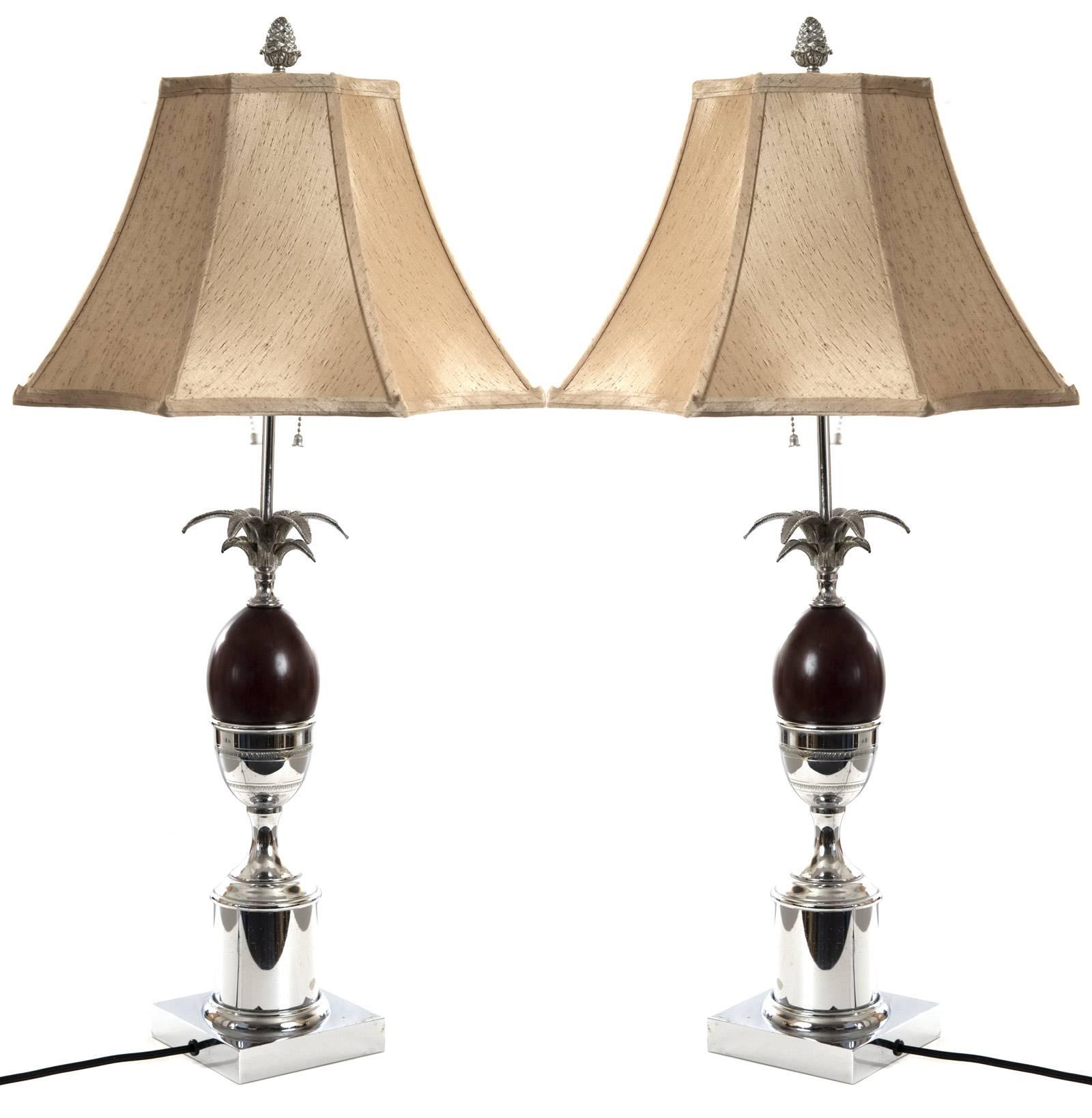 A pair of 20th century Hollywood Regency style table lamps on a square base with a stepped column on which sits an urn holding a wooden ovoid form that is mounted with pineapple leaves, with a chrome neck that supports two-lights. The lamp is fitted