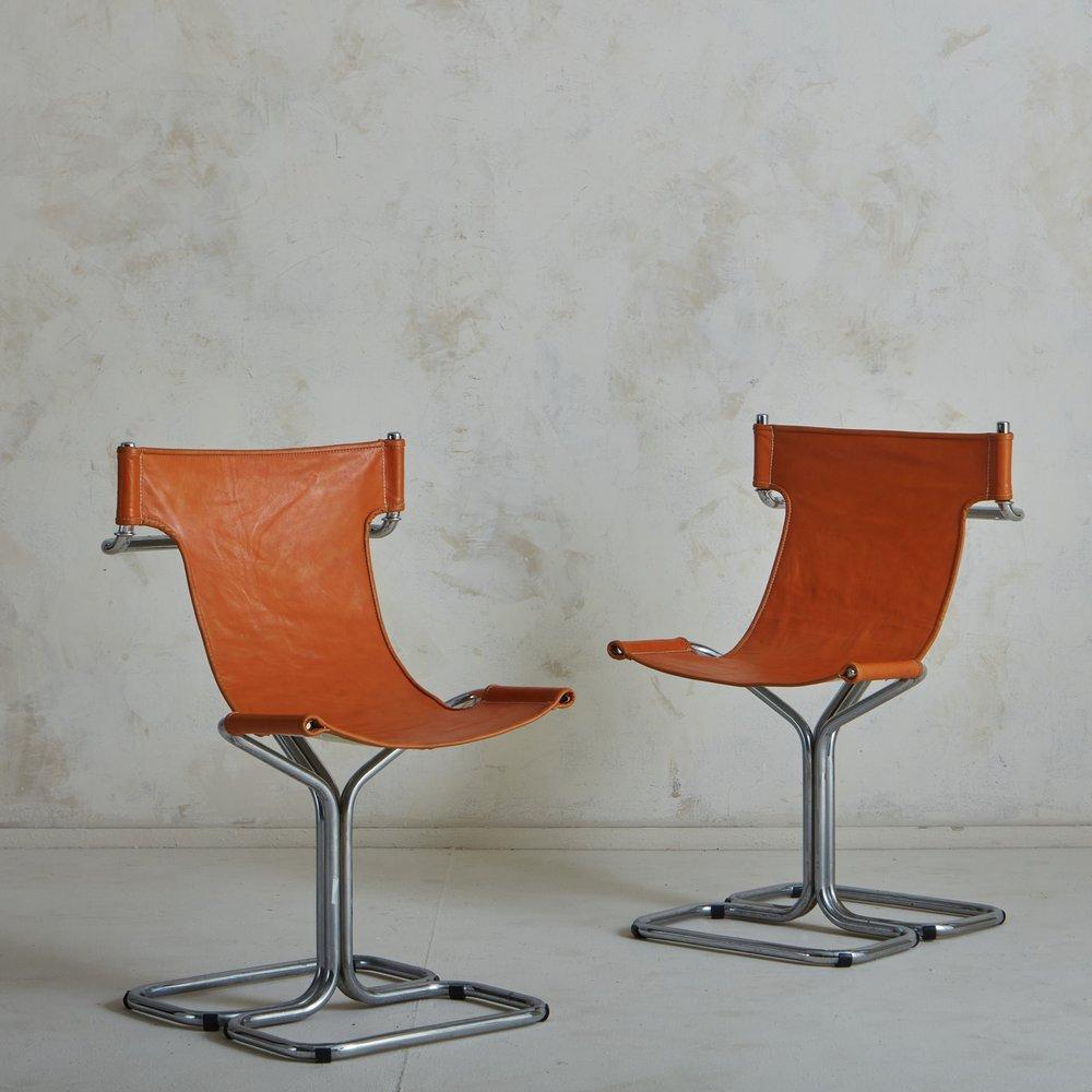 A pair of 1970s Italian accent chairs featuring tubular chrome frames and cognac leather slingback seats with stitch detailing. These chairs are perfect to style with a kitchen table or as accent chairs to float between living spaces. Unmarked.