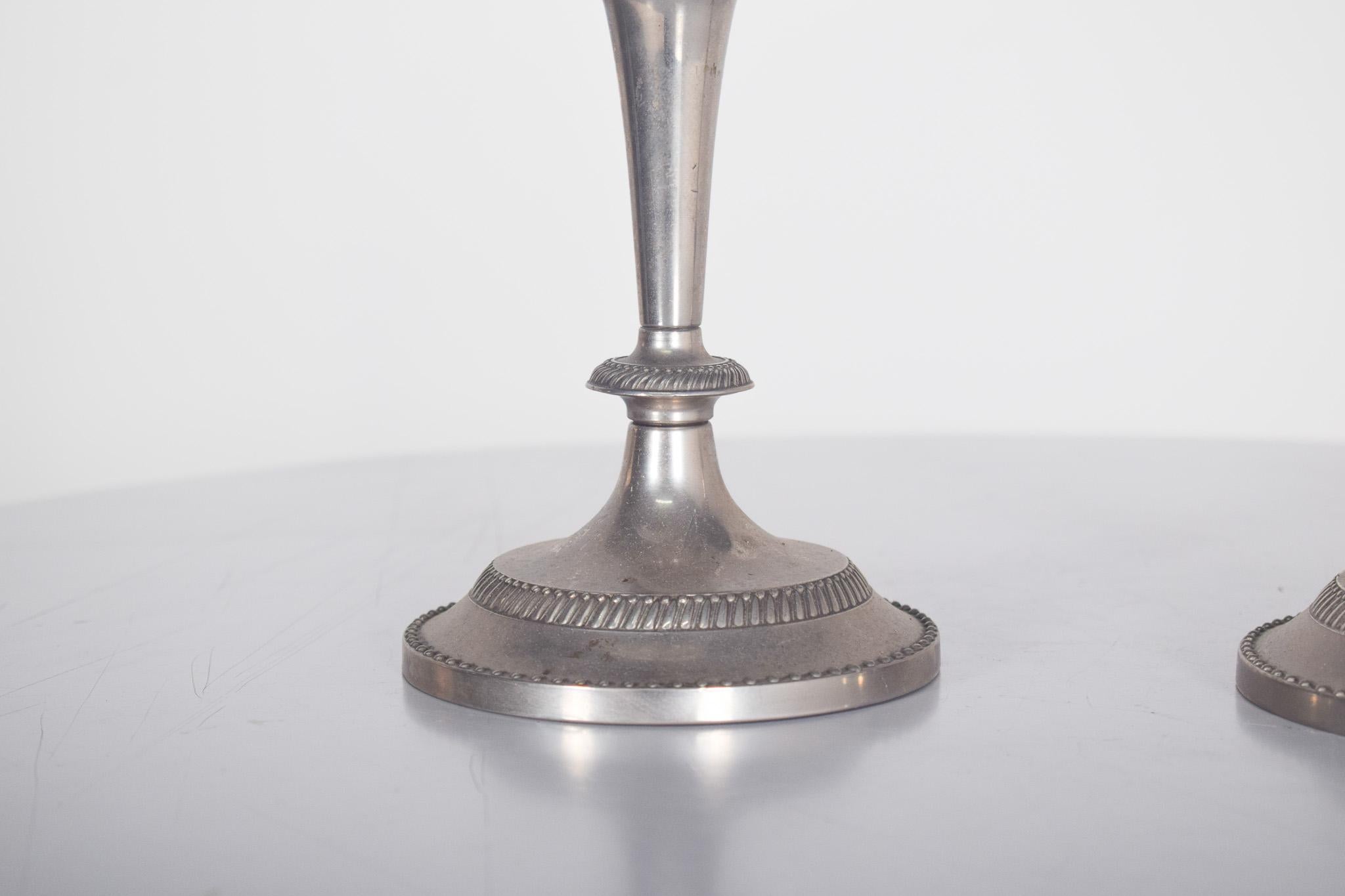 Paire de bougeoirs en zinc chromé, fabriqués en Chine. Arbres en forme de balustre partiellement lisses. Des appliques nacrées et gaufrées qui servent de support aux bougies.
Chaque bougeoir est doté d'une base circulaire robuste décorée d'une frise