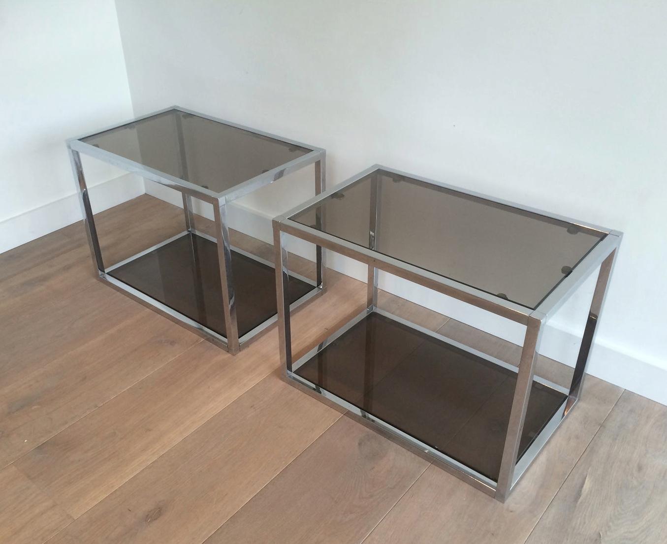 This pair of side tables are made of chrome with smoked glass shelves. This is a French work, circa 1970.