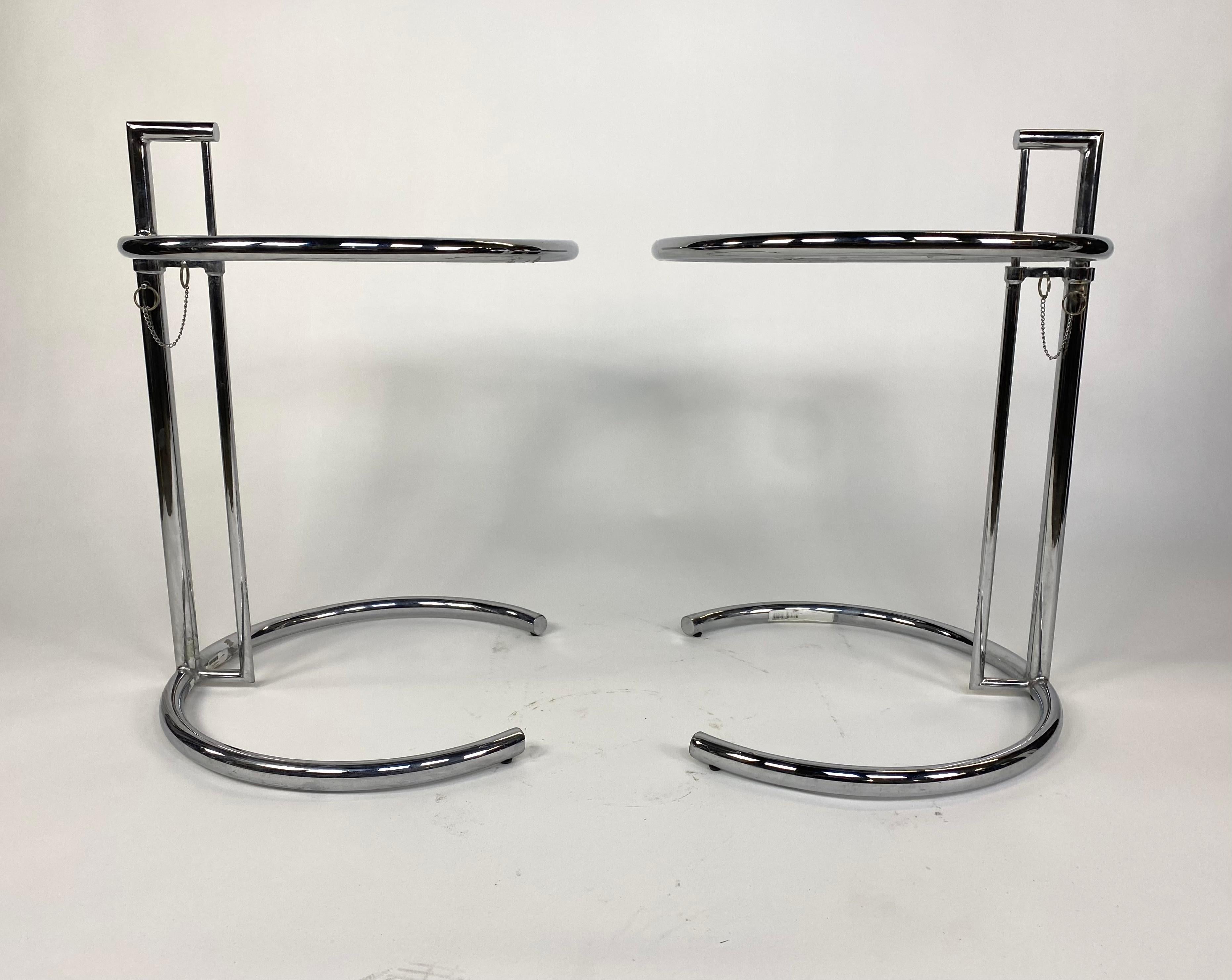 Pair of Mid-Century Modern adjustable height chrome cantilever side tables in the style of Eileen Gray E1027. Single tube chrome with glass table top. Cantilever design allows for variety of uses as a end table, tv table, or bed side tray table. The