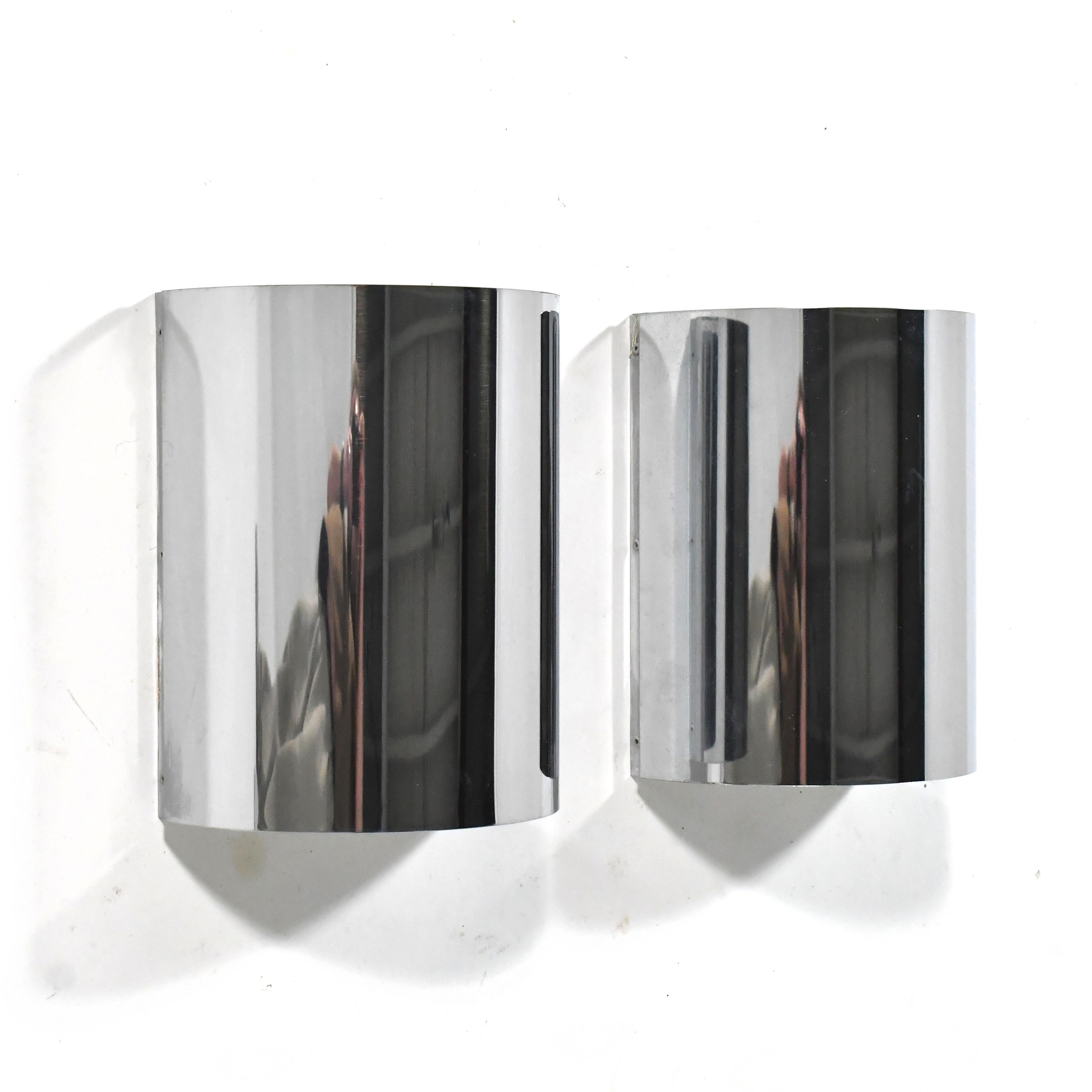 This pair of elegant, minimalist wall sconce lamps feature chrome-plated semi-circular-shaped steel shades concealing two bulb fixtures that cast light upward and downward. They are unmarked other than a model number, but have an aesthetic very