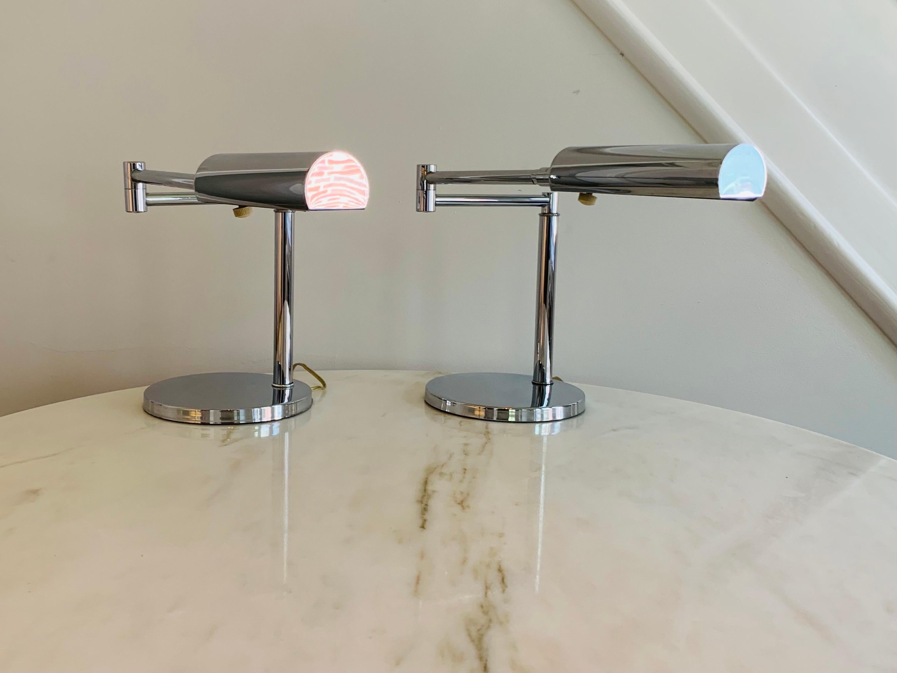 This is a pair of polished chromed-steel desk lamps by Koch + Lowy. The cylindrical shades articulate on ball and socket joints, and further adjust via a swing-arm.

Each lamp measures 8.25 inches long and wide at base, and is 12.75 inches high.