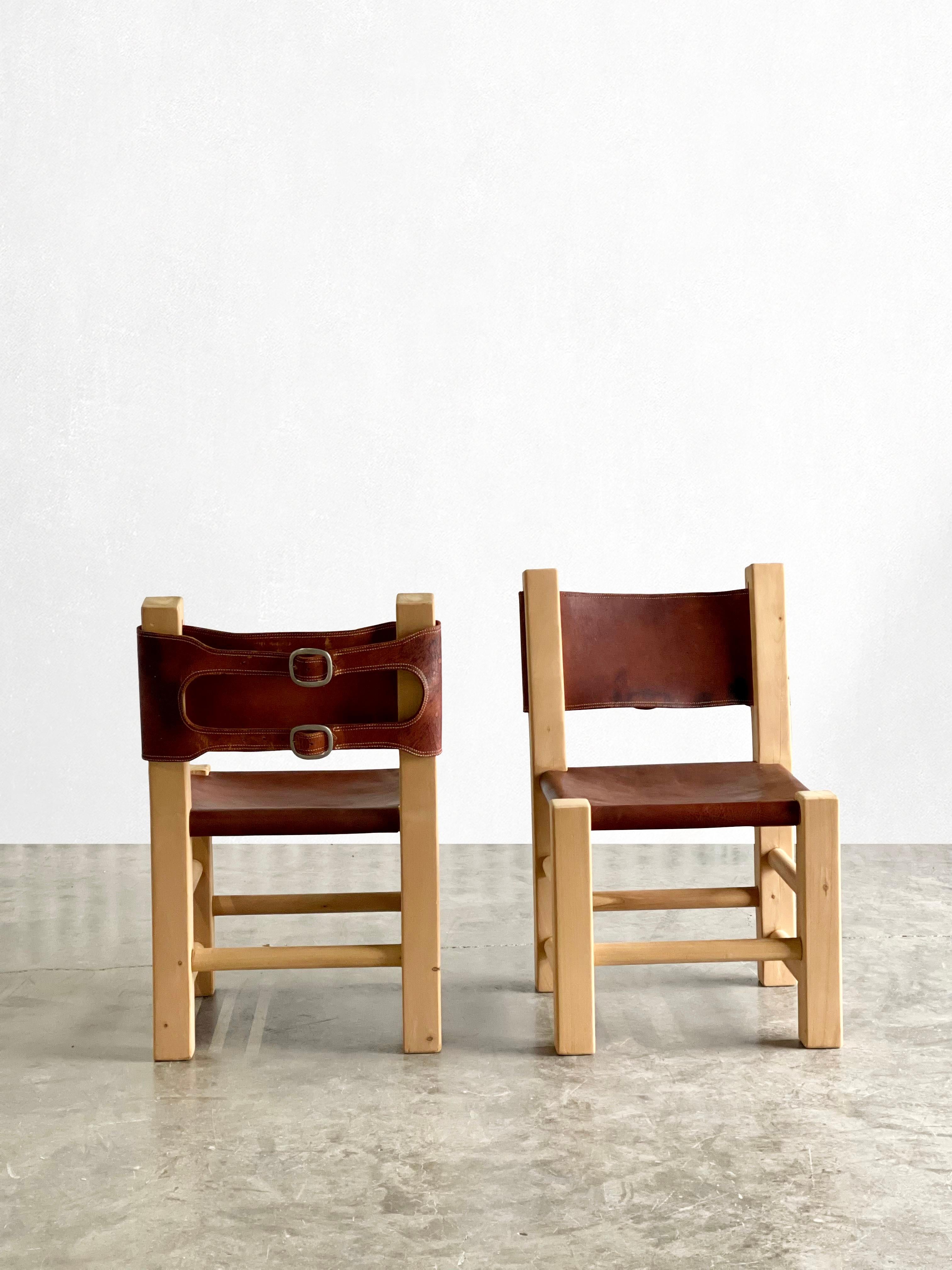 A statement pair of chunky primitive chairs reminiscent of Pierre Chapo. 

These chairs have a solid pine frame that has recently been refinished. Super soft cognac colored leather and smooth pine. The back has a unique buckle detail with