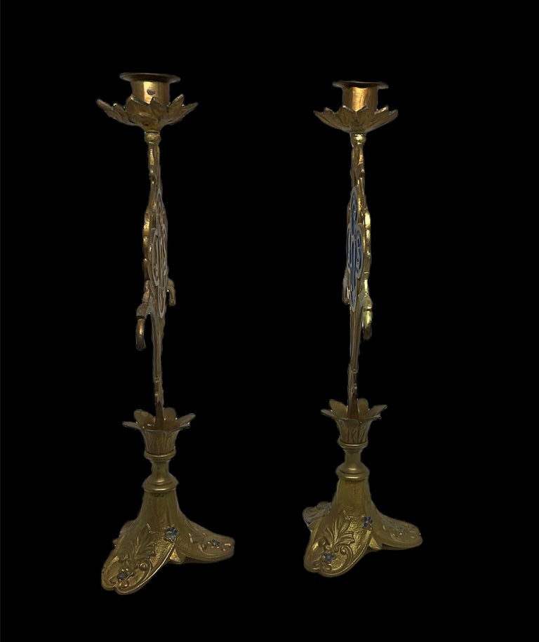 This is a pair of church altar enamel bronzed metal candle holders. Their bases are shaped as trefoils. They have a bas-relief foliage with tiny blue enamel flowers. Above them, there is a five petals flower from where two branches of acanthus