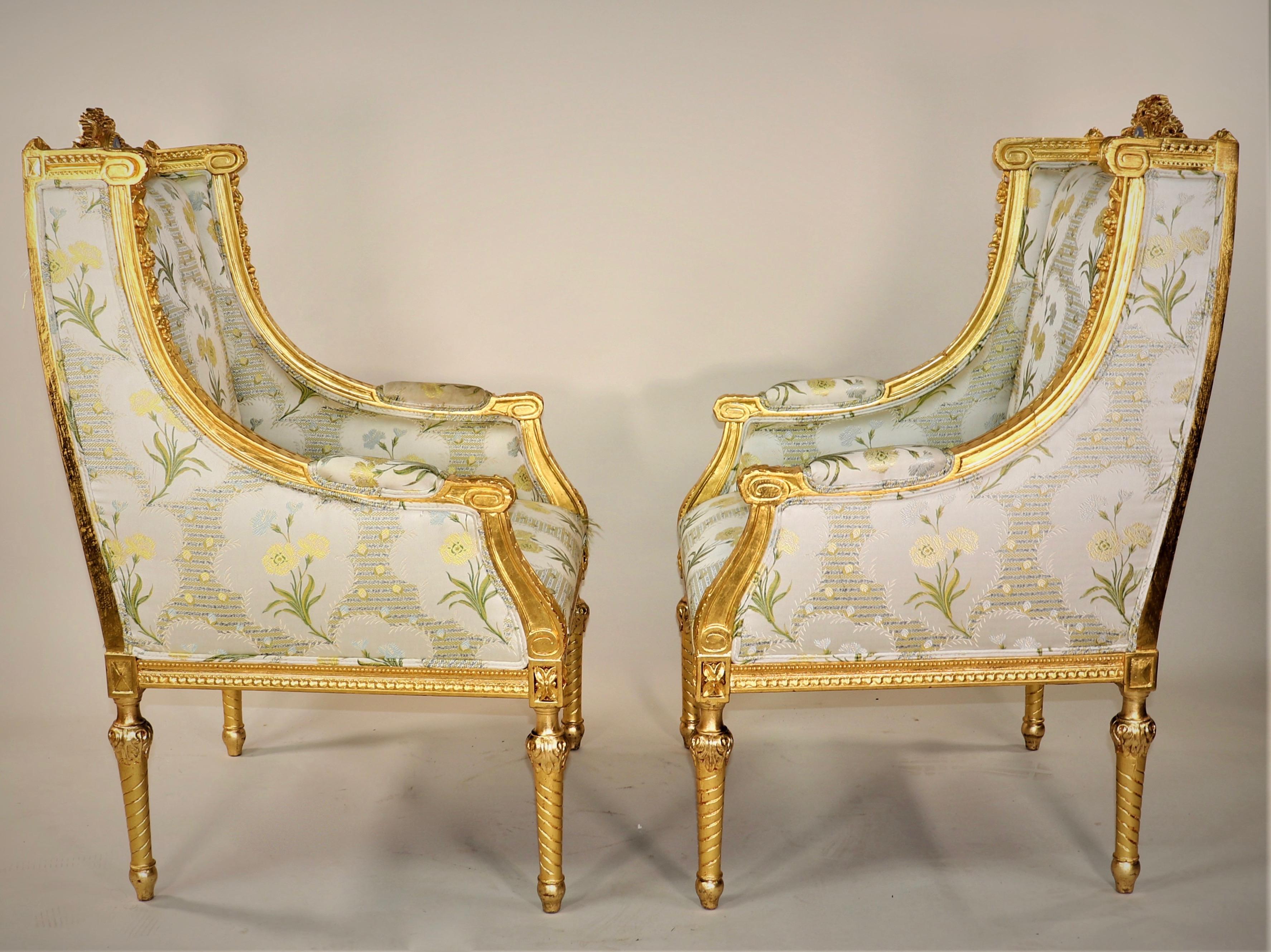 A pair of Circa 1900 French Louis XVI Style Gilt armchairs. This majestic pair of chairs has a beautiful green floral silk embroidered fabric with a luminous gold gilt wooden frame. Each chair has a jasperware medallion crowing the top of the backs.