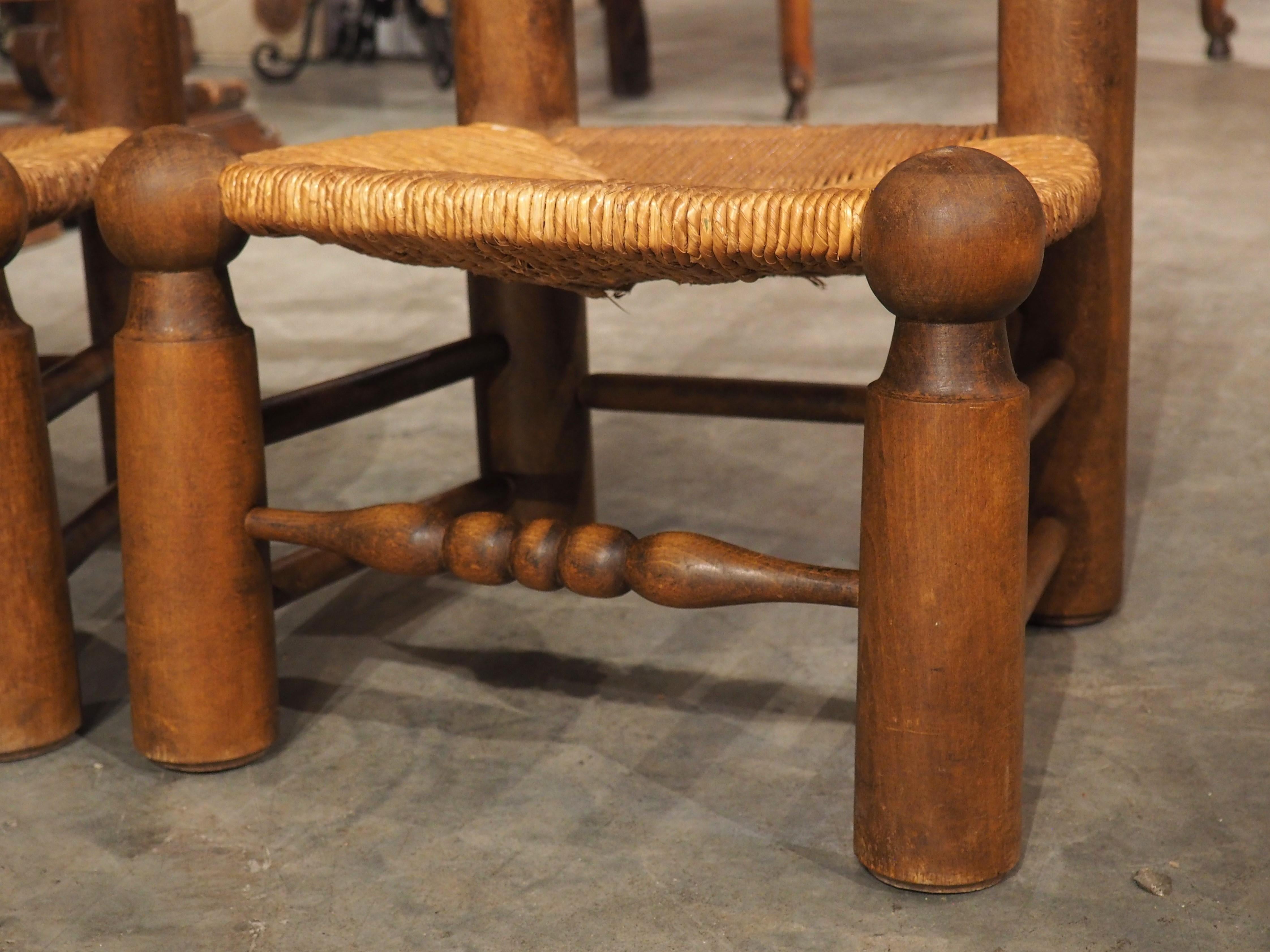 In the style of Charles Dudouyt (1885-1846), a famed French woodworker whose designs are noted for their use of natural materials (in this case, beech and straw) and minimalist carvings, this pair of low fireplace chairs were hand-carved circa 1940