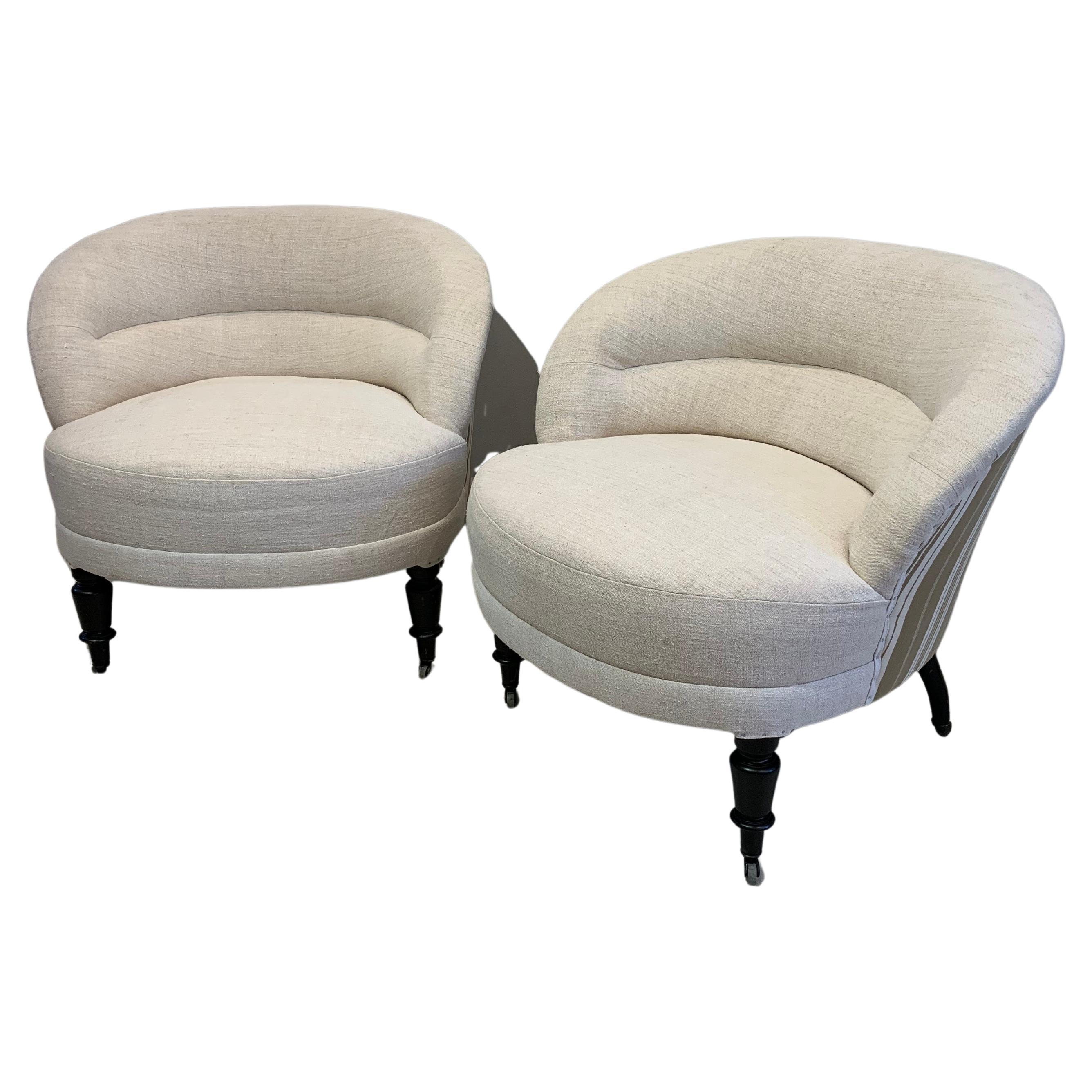 A pair circa 19th century Napoleon III comfortable and substantial upholstered armchairs covered in neutral slubby French linen with a contrasting antique french ticking at the back.

The lounge chairs feature curved low backs and typical ebonised