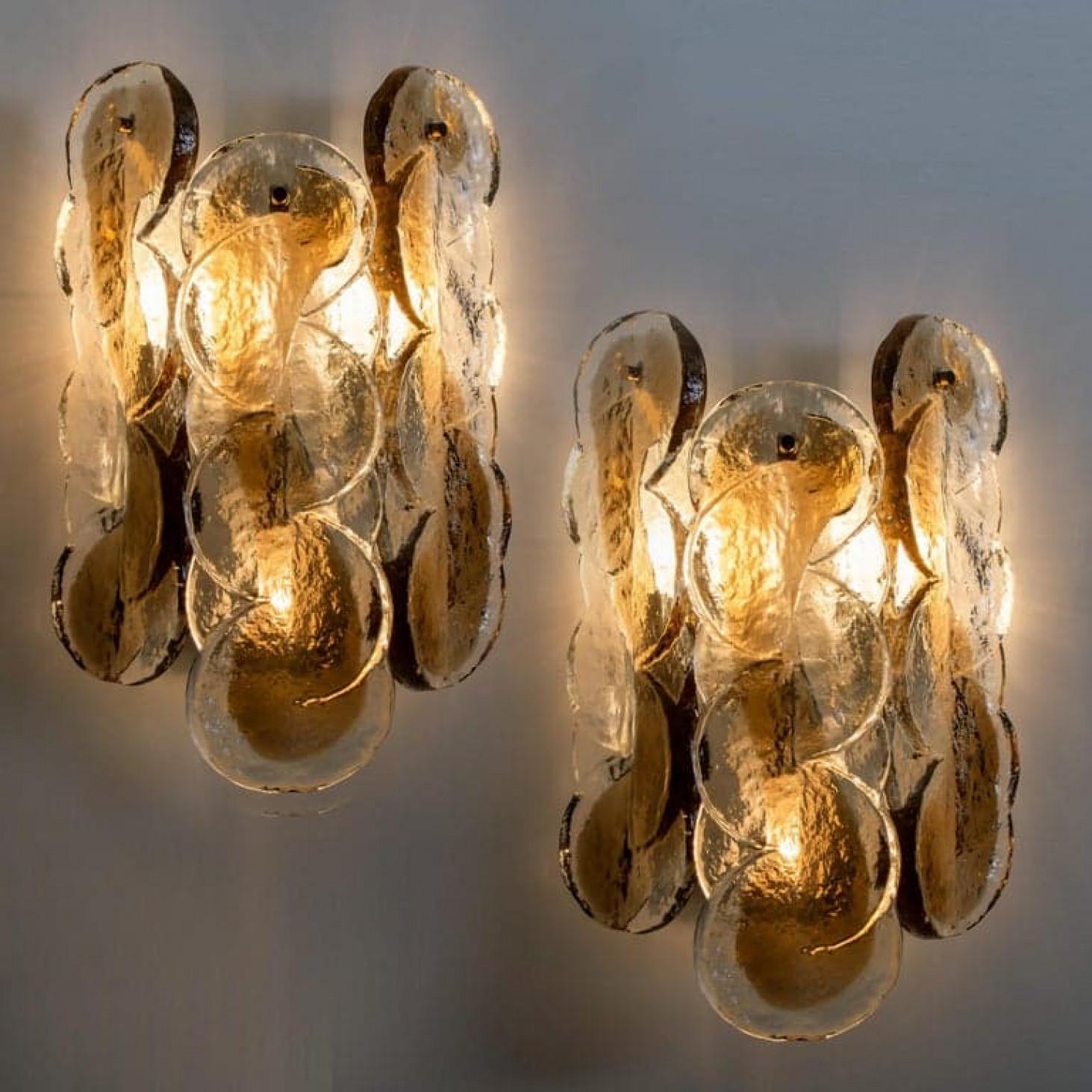 Pareja de apliques de pared Kalmar con ligero remolino de color ámbar dorado. El hermoso cristal de textura gruesa se complementa con los herrajes cromados. Diseño sencillo y limpio. Vidrio fundido soplado a mano, de vidrio ahumado y transparente.