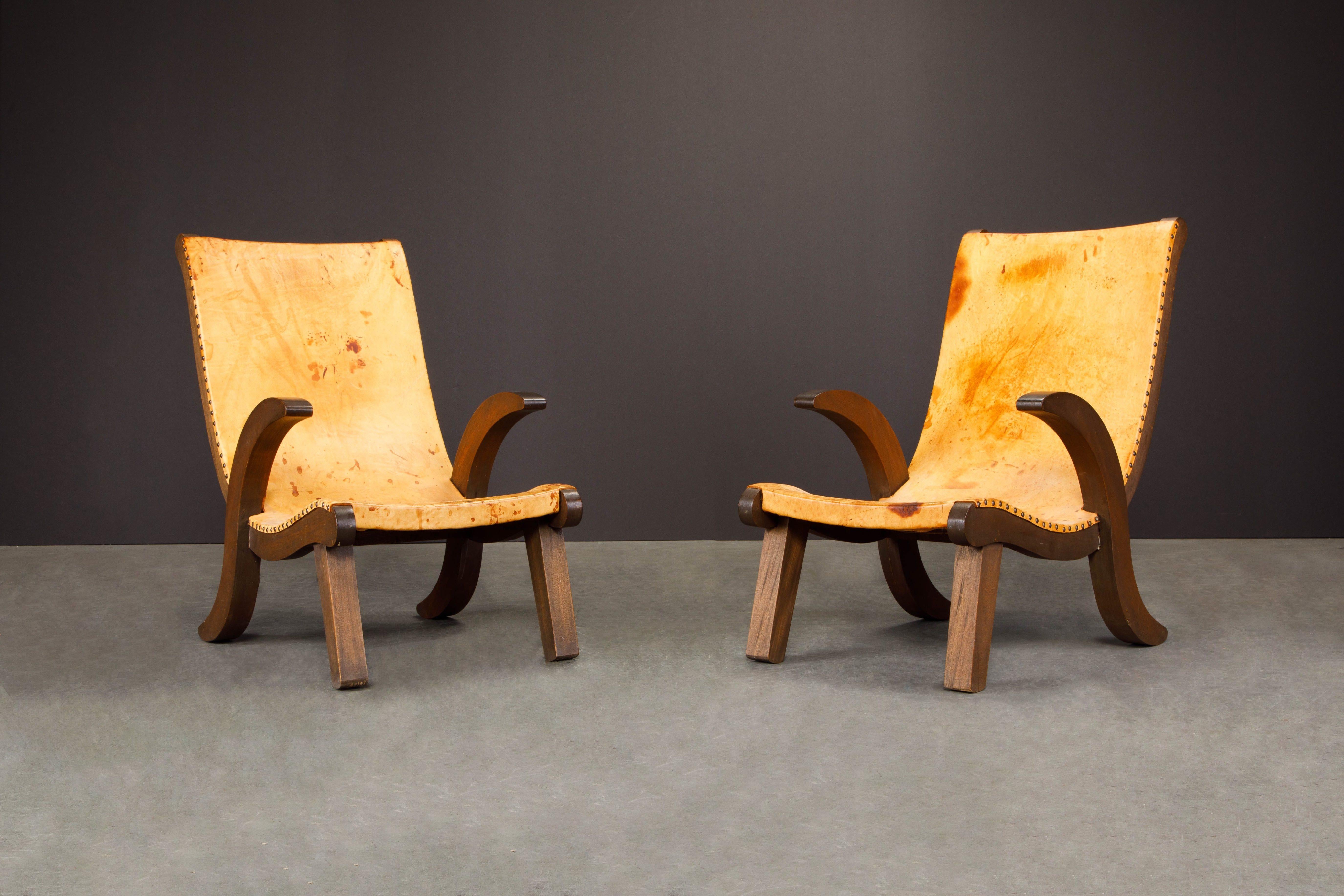 This beautiful pair of Clara Porset style Butaque chairs are in gorgeous aged leather, stained wood and brass rivets. These incredible lounge chairs are as comfortable as they are stylish with thick aged saddle leather sling seats attached with