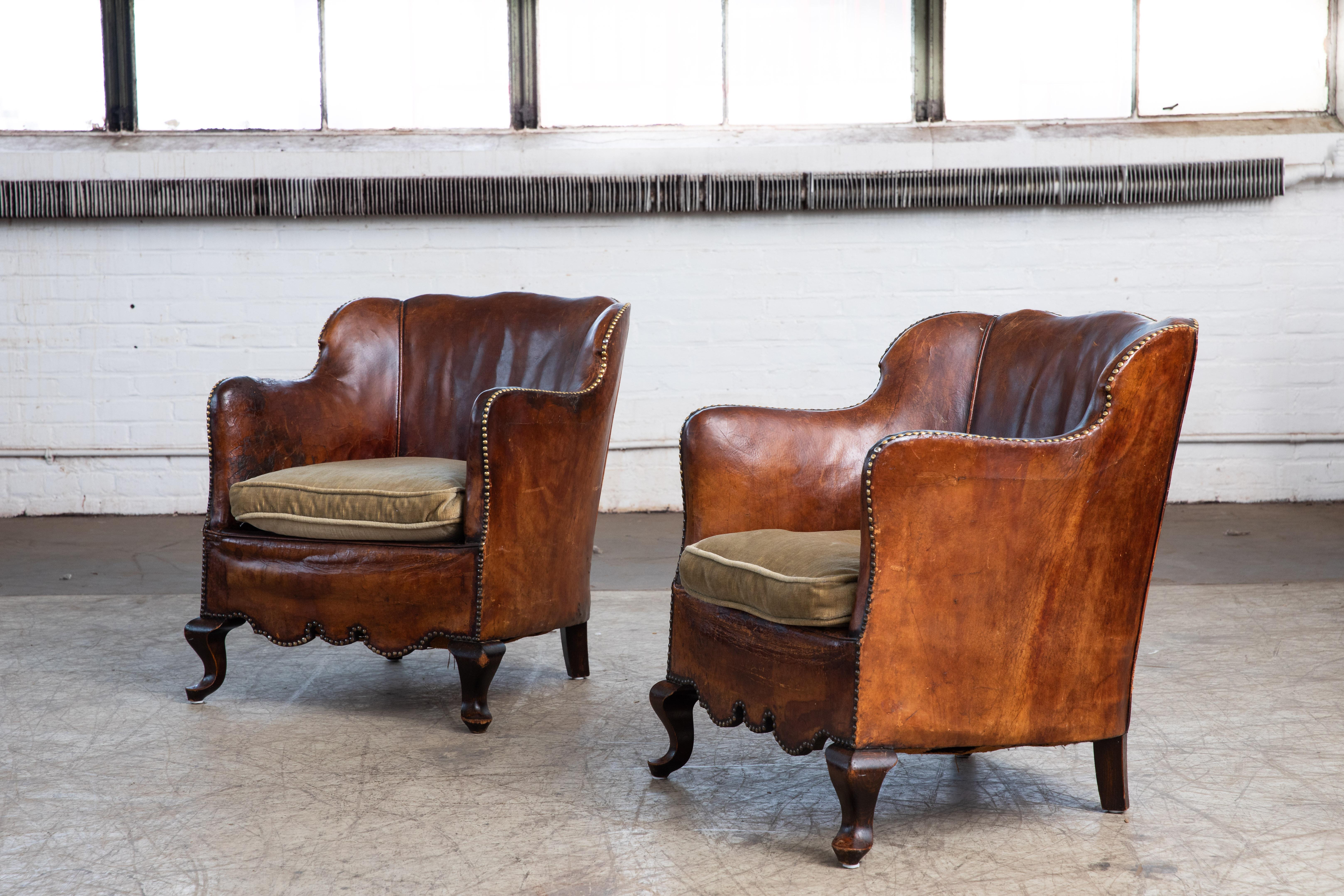 Charming pair of small scale Danish club armchairs attributed to Danish Furniture Maker Oskar Hansen made around the mid-1930s. Covered in original cognac brown leather with a smooth back and brass nail accents. Fantastic color and a lot of noble