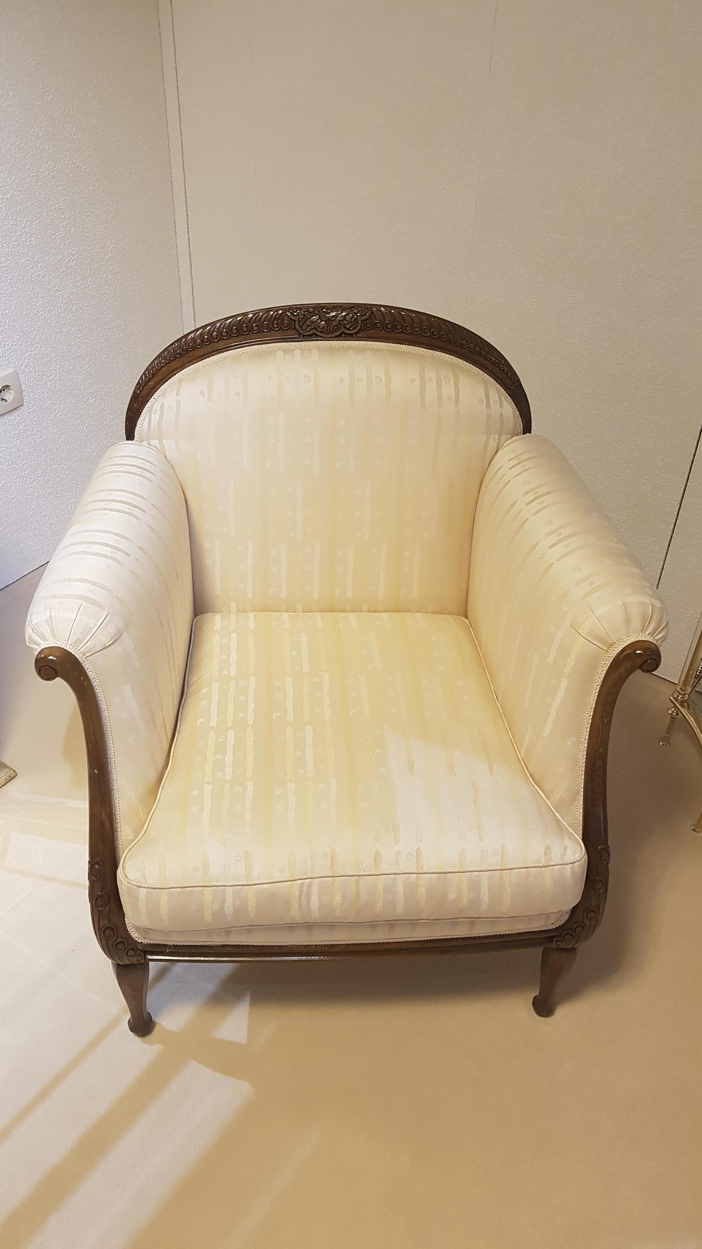 Two Classic design armchairs made of elegant and massive dark walnut wood and covered with a high end crème white fabric. The wood part features beautifully carved ornamentation while the fabric offers small stripe details. Comfortable cushions all