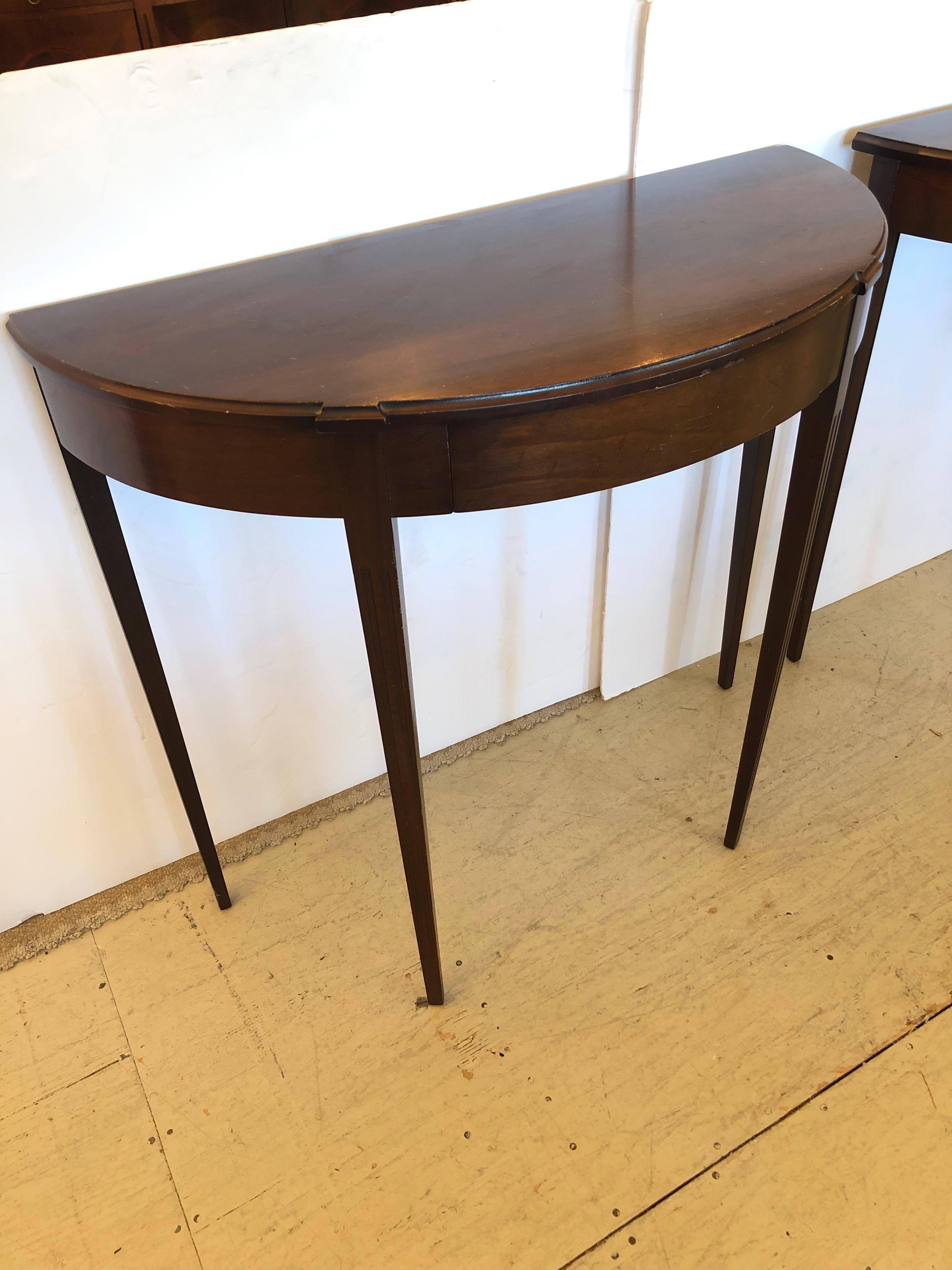 Refined pair of mahogany Hepplewhite style demilune shaped console tables having lovely tapered legs and classic simple elegance.