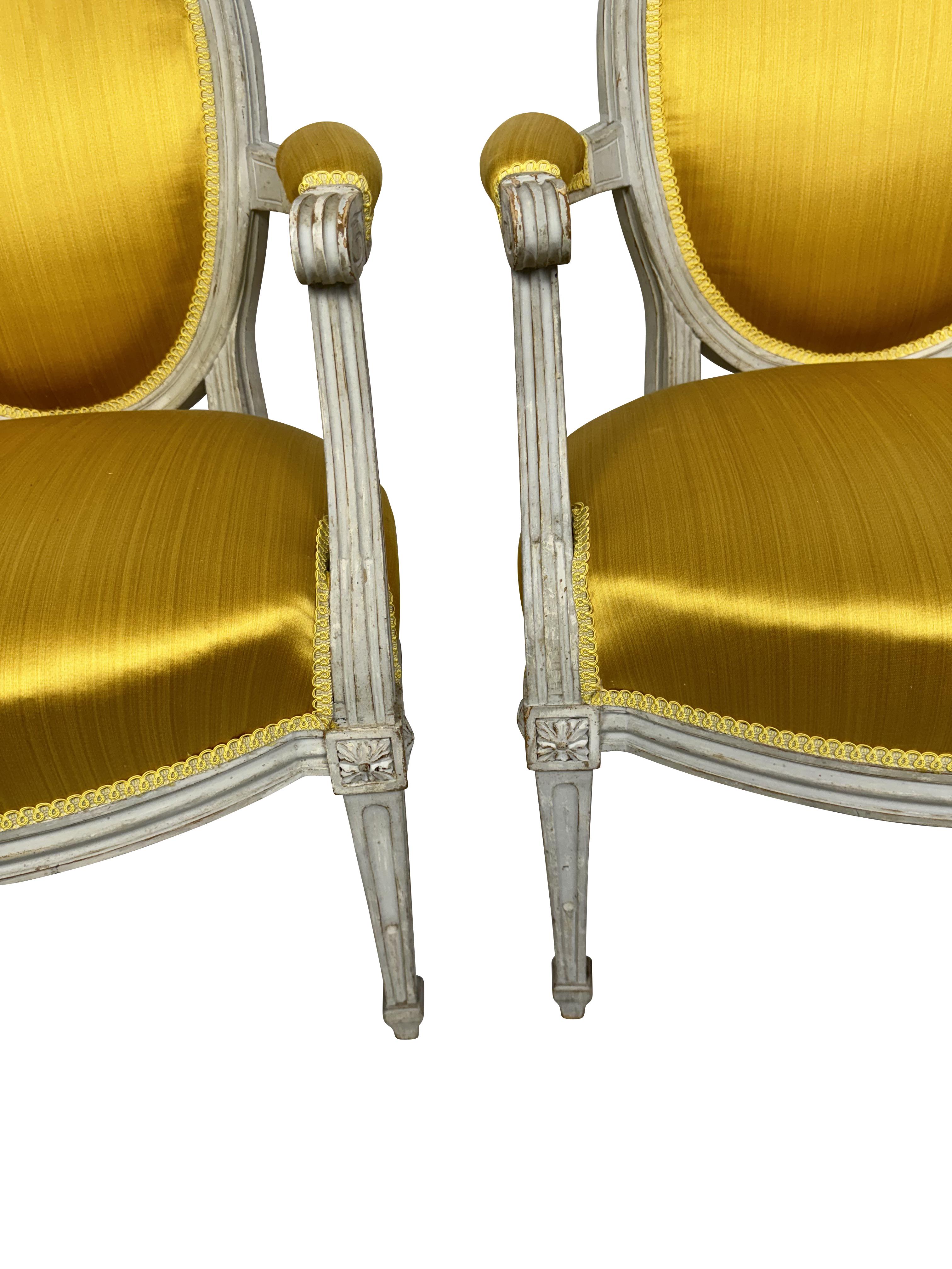 Paire de fauteuils Louis XVI robustes avec cadres peints crème/blanc et tapisserie jaune d'or. Les pieds sont ornés de fleurons sculptés et les pieds fuselés classiques de style Louis XVI sont cannelés et se terminent par des pieds toupies.  Tous