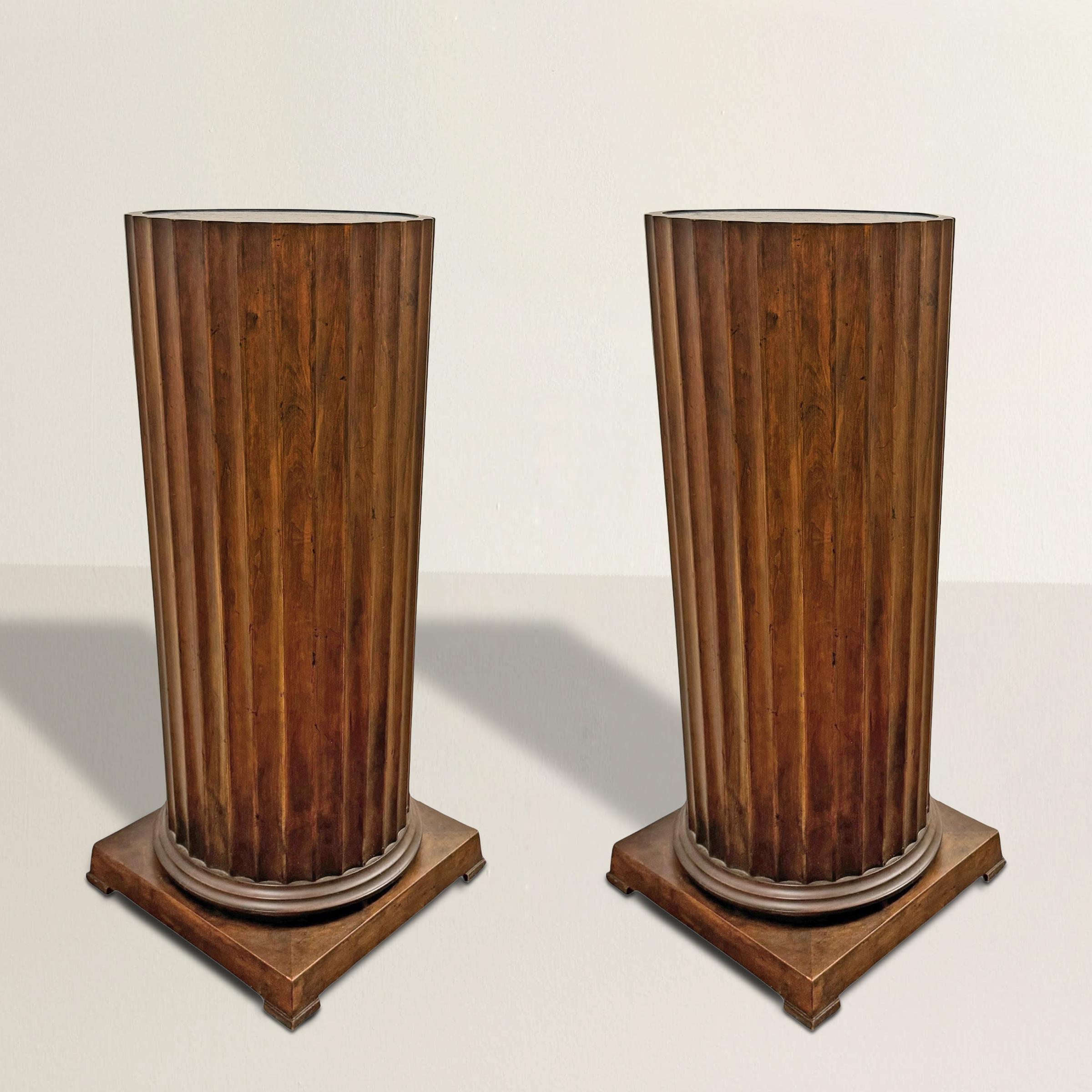 A striking fusion of sculpture and utility, this pair of mid-20th century American pedestals brings the grandeur of antiquity into the present. Crafted in maple and finished with a deep walnut stain, their fluted forms echo classical columns, while