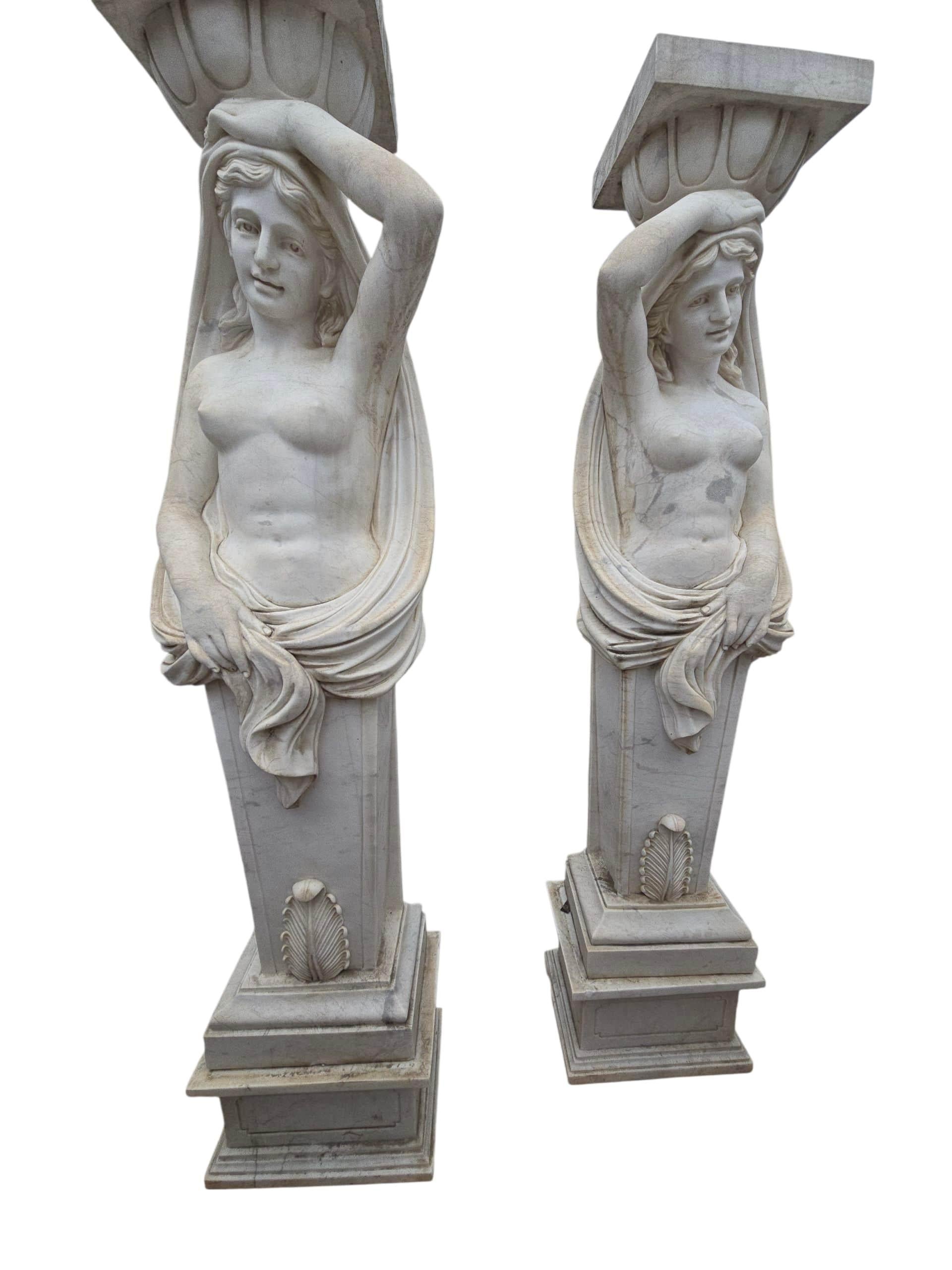 Elegante coppia di sculture femminili classiche scolpite in pregiato marmo italiano di Carrara, realizzate in Italia negli anni Ottanta. Ogni figura è raffigurata in un'aggraziata posa greco-romana, con drappeggi fluenti ed espressioni serene,