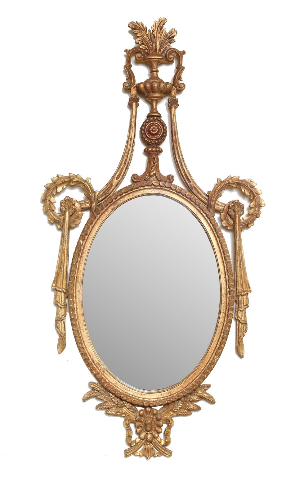 Pair of mirrors, in richly carved giltwood frame, each having an oval mirrorplate, with border of gadrooning, surmounted by elaborate pediment of acanthus-filled urn, over rosette, flanked by swags and scrolls, its base adorned by wheat, ribbons,