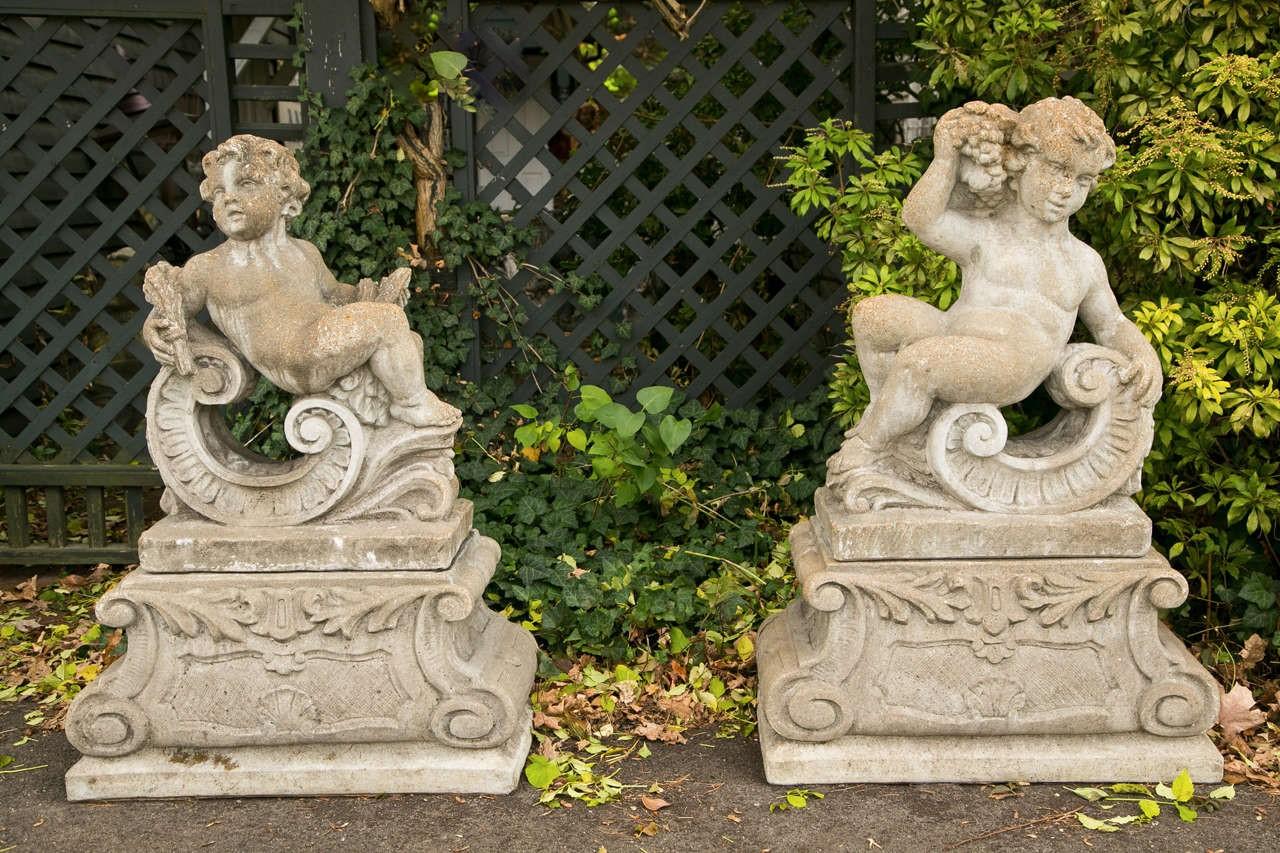 Klassische Gartenstatue mit Putten, die zwei der vier Jahreszeiten darstellen. Die steinernen Kompositstatuen stellen einen Cherub mit lockigem Haar, großen Augen und runden Wangen und nacktem Körper dar, der den Weizen für den Sommer und die