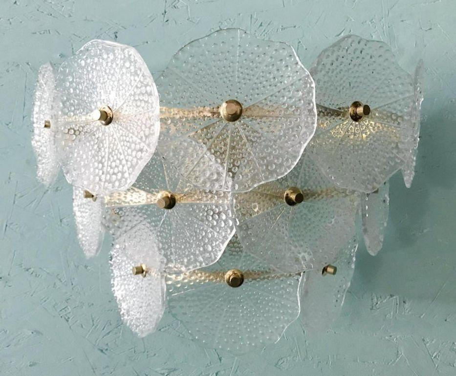 Elegante coppia di appliques in vetro di Murano degli anni '80 con paralumi in vetro chiaro soffiato a mano a forma di petalo montati su telai in ottone lucido. Gli elementi scultorei in vetro diffondono delicatamente la luce, creando un ambiente