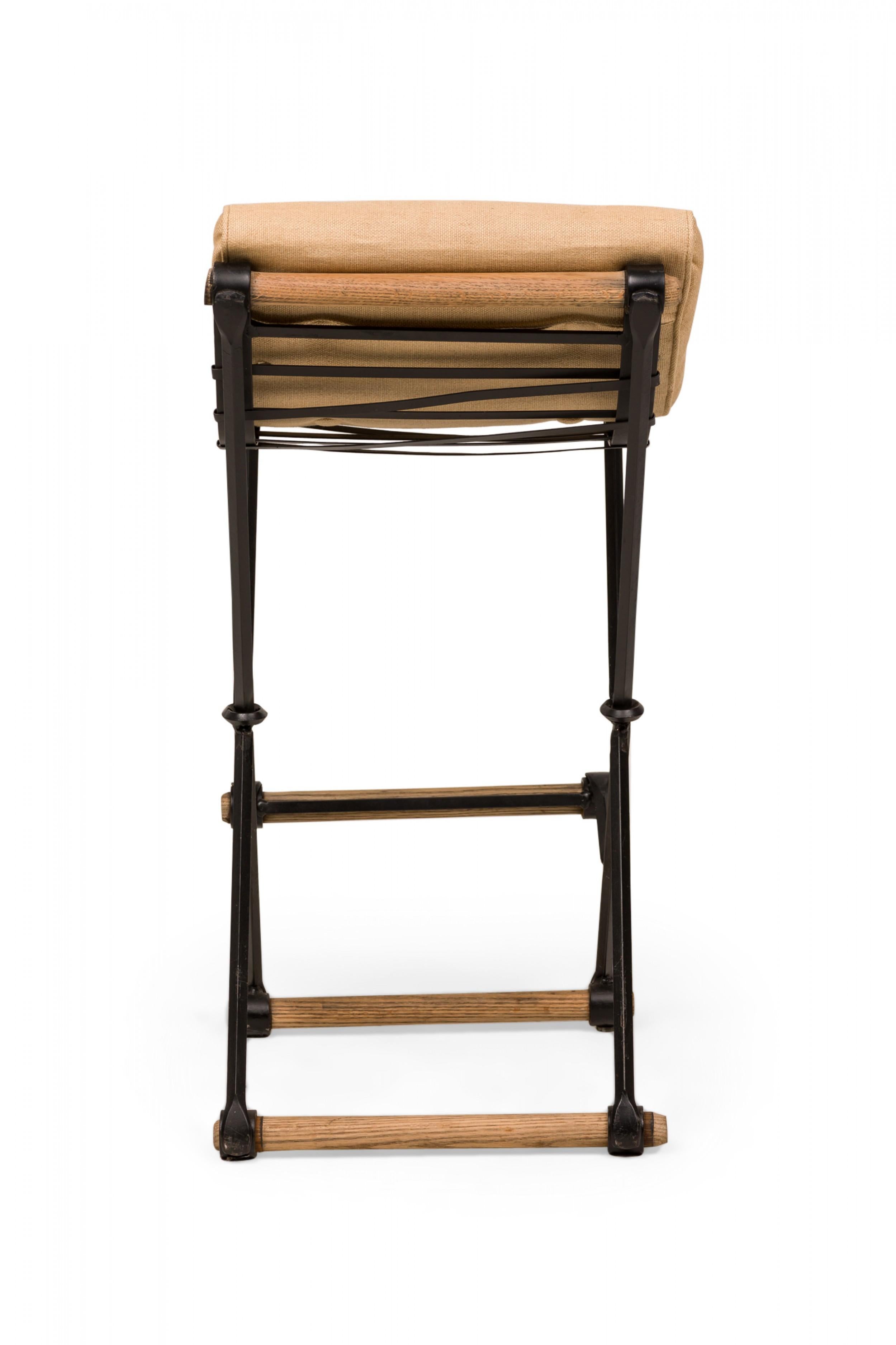 Pareja de taburetes de bar americanos de mediados de siglo (años 70) con estructura en X, con cojines de asiento tapizados en tela tejida beige con detalles de botones, que descansan sobre robustas estructuras de hierro y roble. (CLEO BALDON PARA