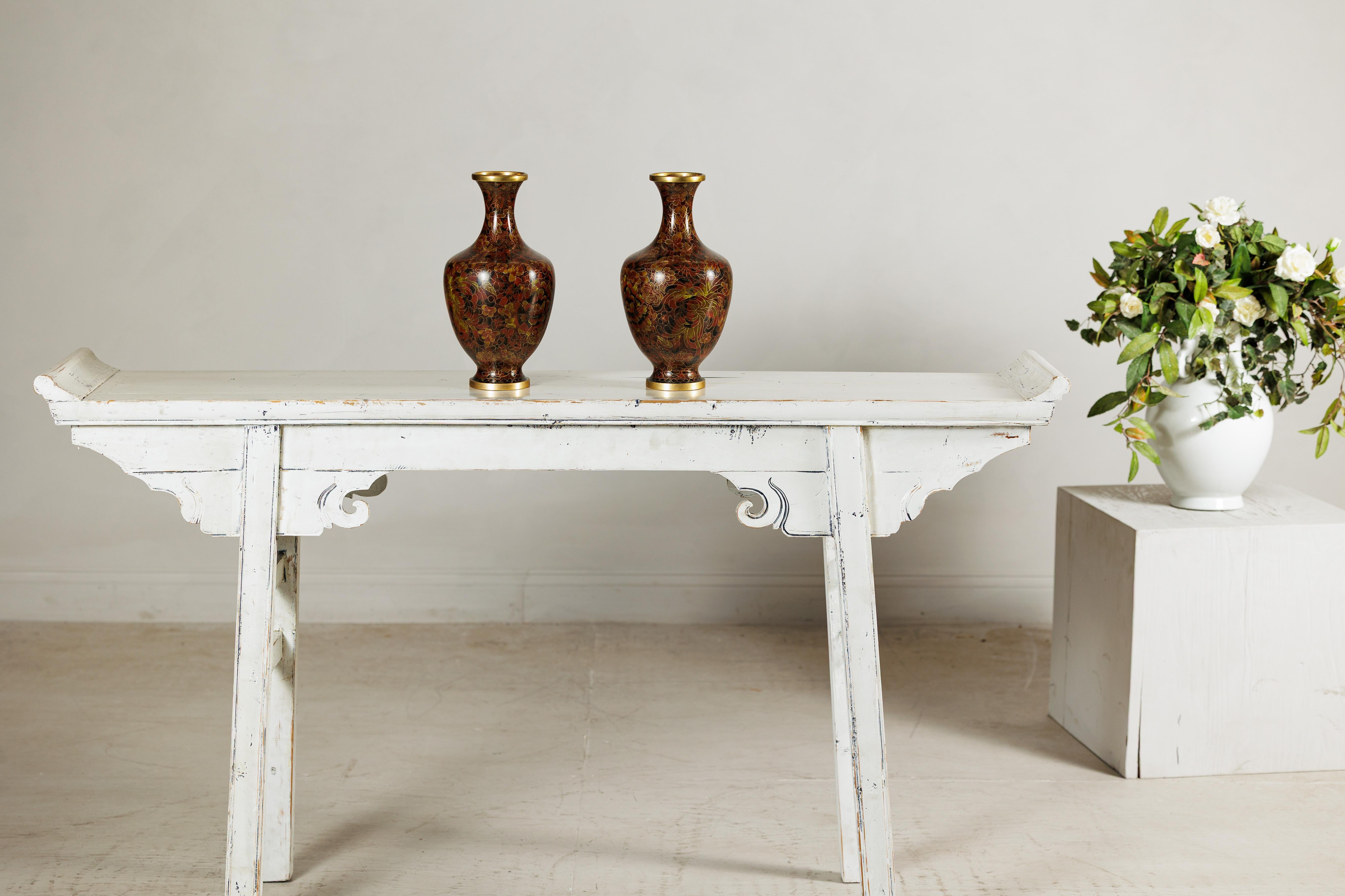 Cette paire de vases cloisonnés offre un accent décoratif raffiné avec leur fond brun-rouge chaud enrichi de motifs floraux complexes de couleur rousse, ocre et or. Les gracieuses silhouettes balustres s'élèvent vers des bords évasés dorés et