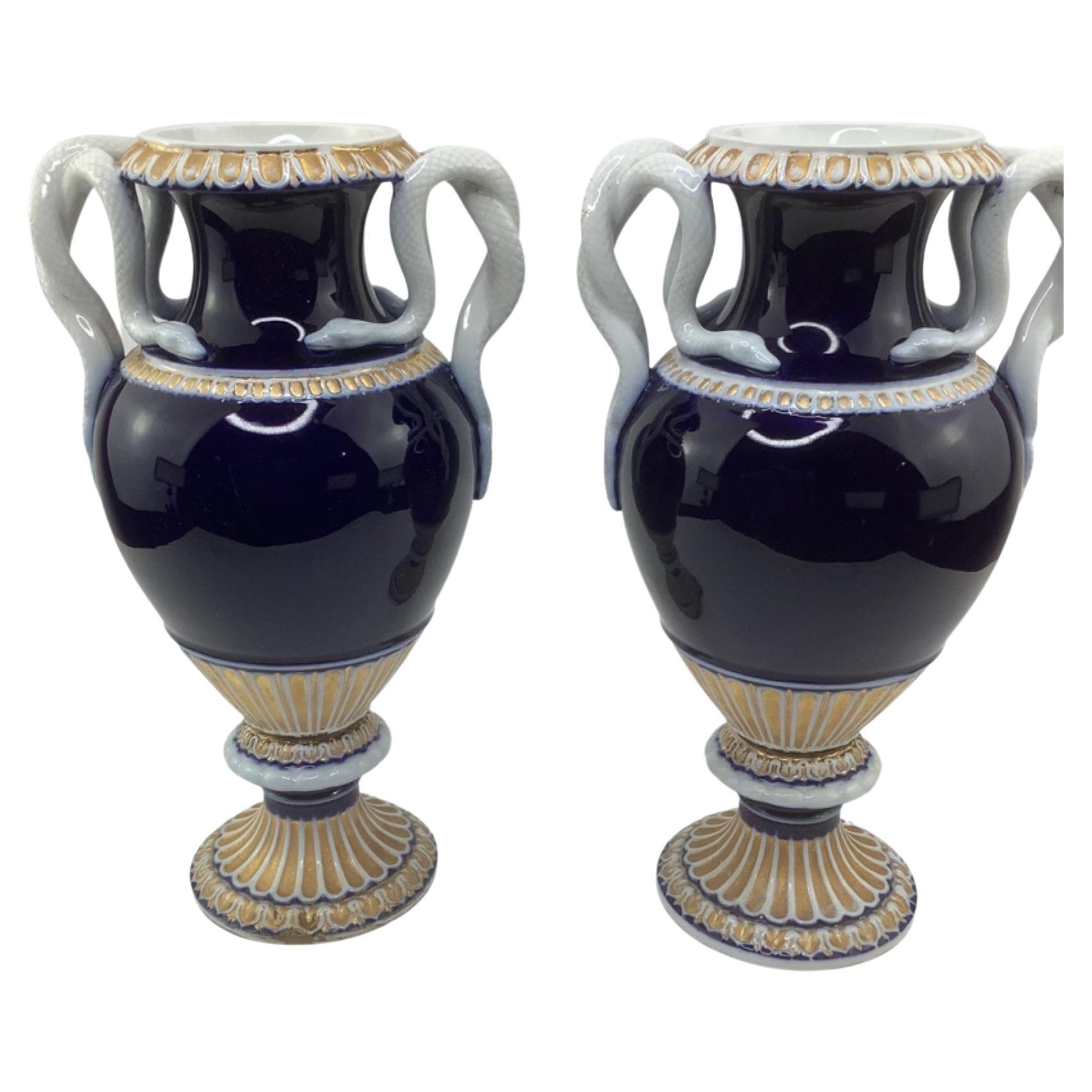 Pair of 19th century cobalt blue Meissen serpent vases in the Neo-Classical style. Boldly colored cobalt urns with white intertwined double scrolled serpent handles. Urns sits atop round gilt accented bases. Exceptional quality with Meissen crossed