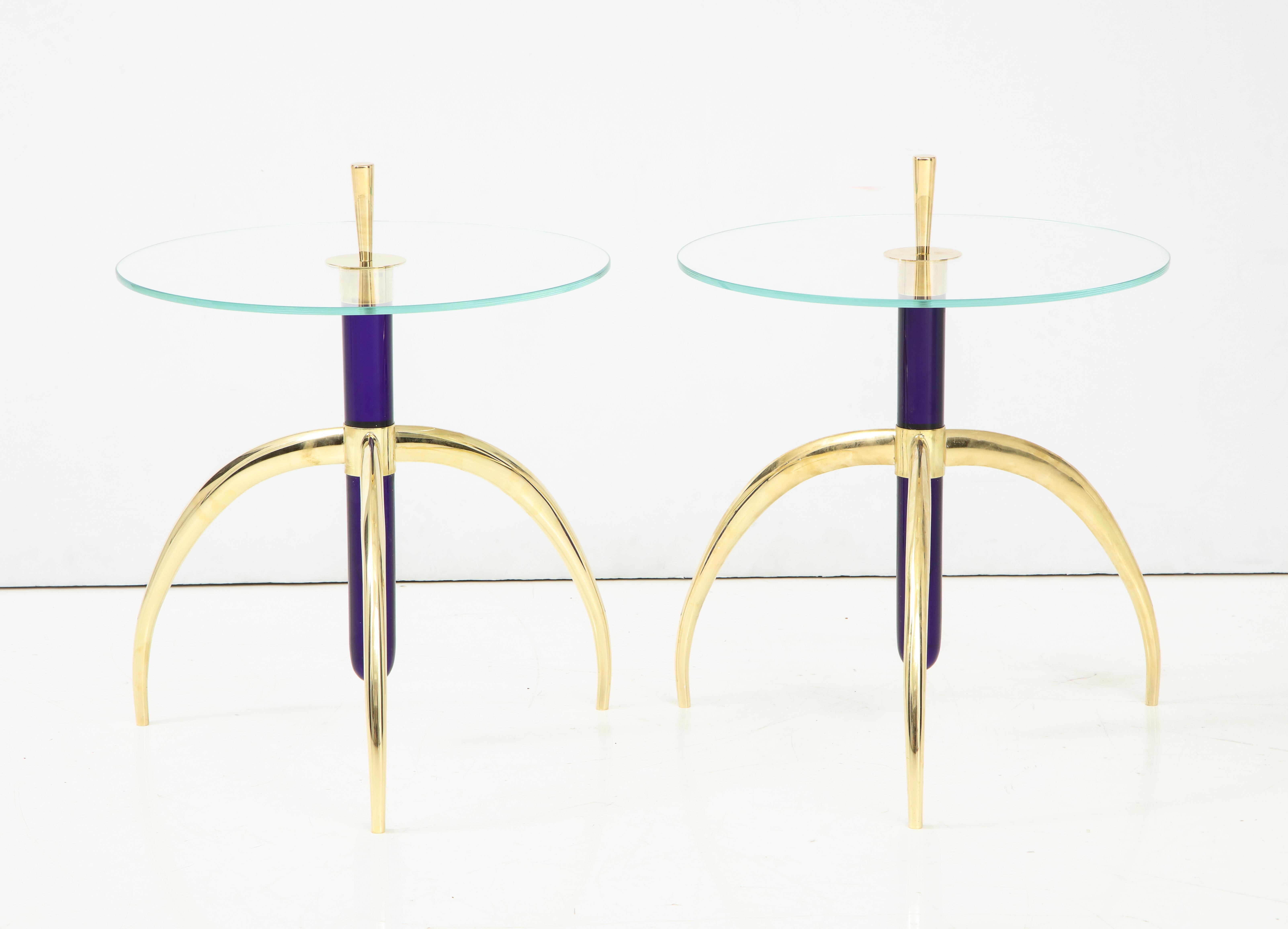 A pair of Italian side or end tables, the circular glass top pierced with a large brass finial connecting thick vintage cobalt blue Murano glass tubular columns supported by contemporary curved brass tripod bases.