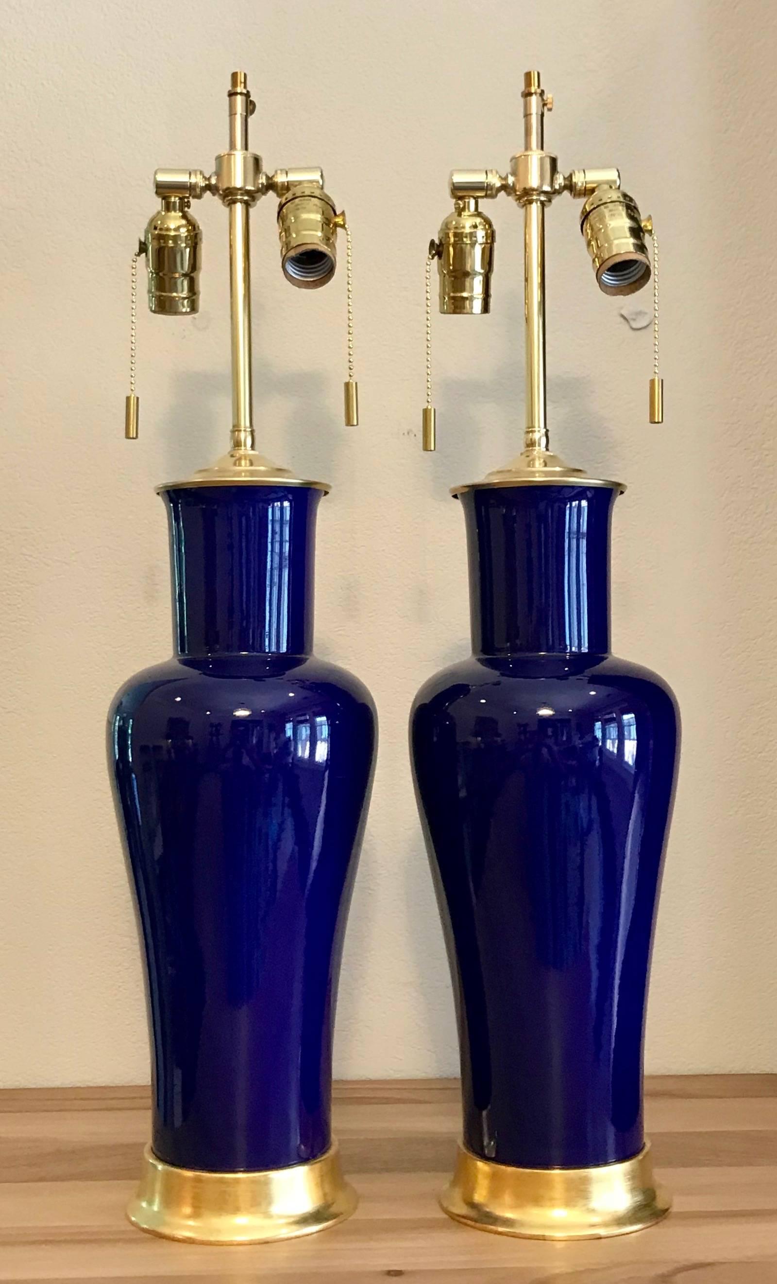 Pair of beautifully crafted porcelain lamps in a vibrant cobalt blue with reflective glaze. Mounted on custom 23 karat water gilt turned wood bases. Wired for US with on/off pull chain sockets, brass fittings and French style rayon covered twisted