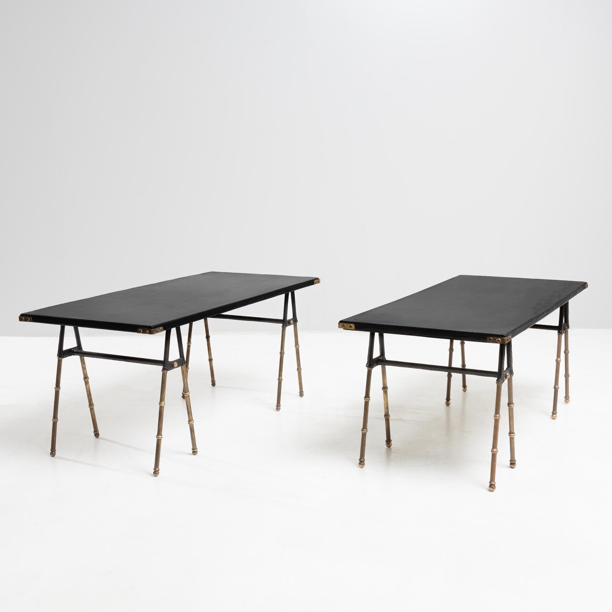 Elegant pair of coffee tables by Jacques Adnet with tops entirely covered in black leather, bronze corner protectors.
The trestle legs screwed to the reverse, in bronze imitating bamboo, the upper elements of which are covered in saddle stitched
