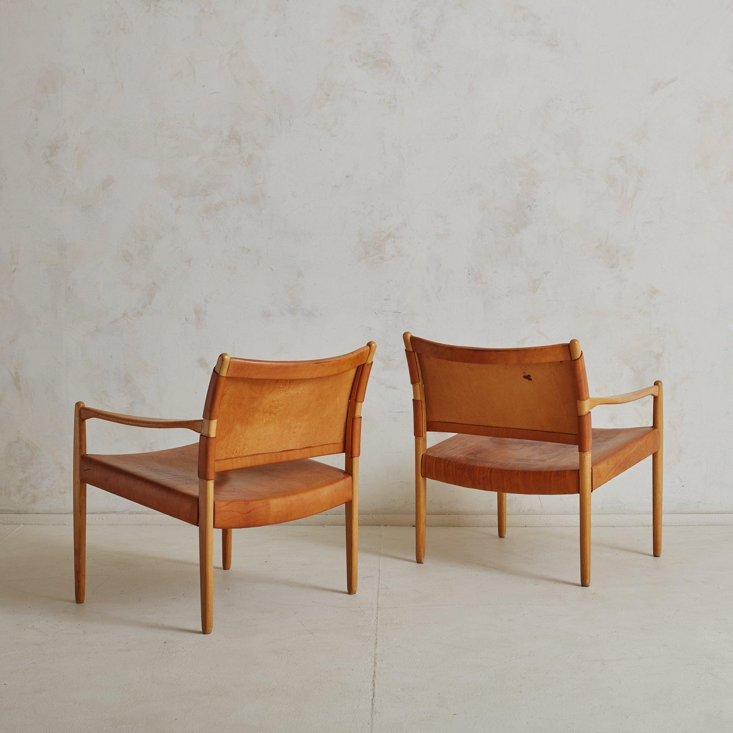 Paire de fauteuils 'Premiär 69' en chêne et cuir, conçus par Per-Olof Scotte pour Ikea en 1967. Ces fauteuils modernes suédois sont dotés d'une structure minimaliste en chêne massif, d'une assise en cuir de selle patiné cognac et d'un dossier