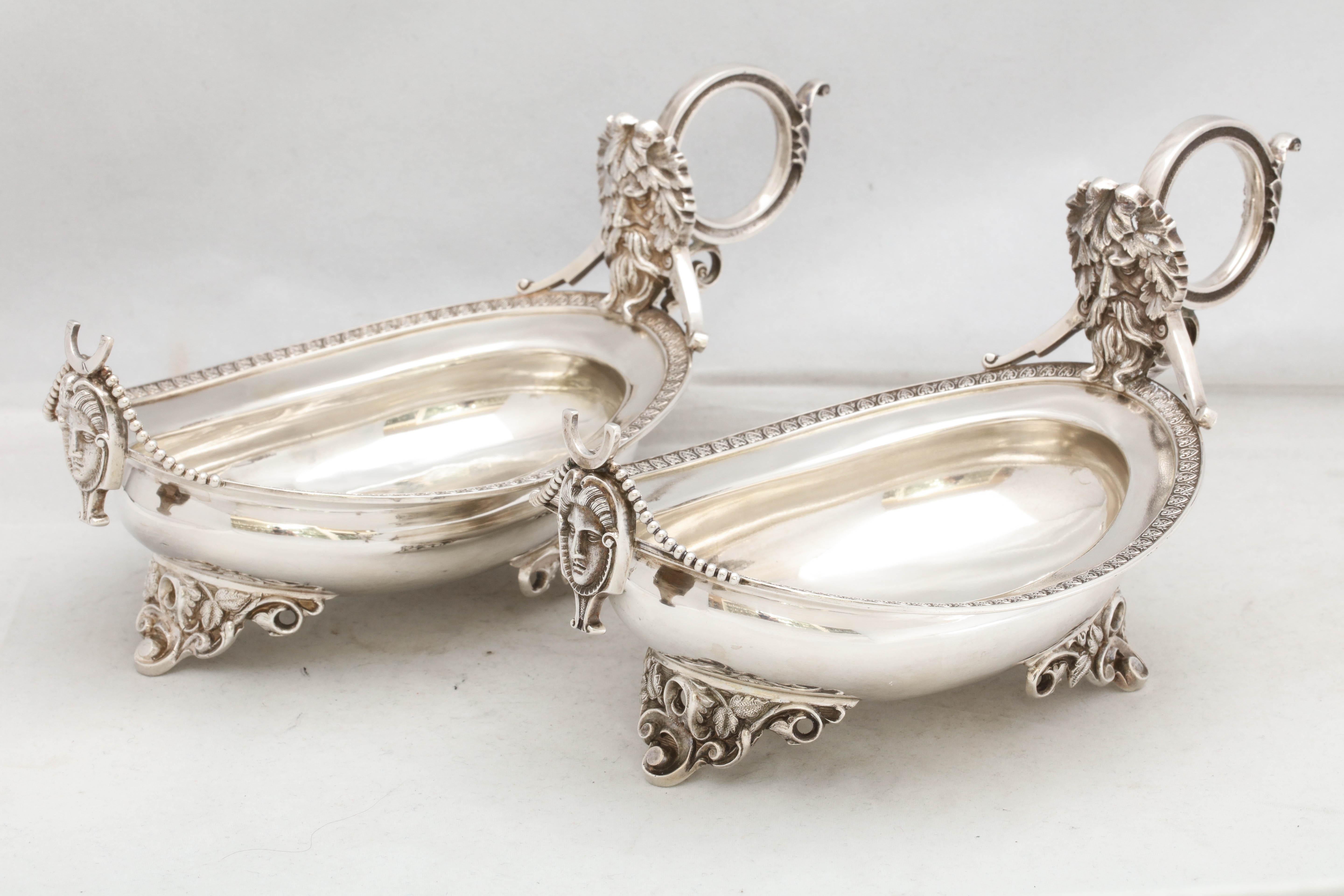 Pair of American, neoclassical, coin silver, footed sauce/gravy boats, New York, Wood and Hughes - makers, circa 1870. The handle of each sauce/gravy boat terminates in a bearded, man's head. A woman's face is at the outer, opposite end of each