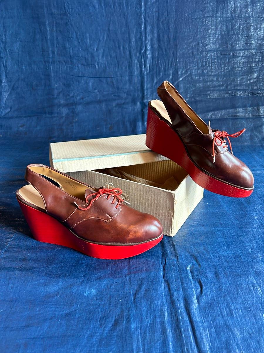 Circa 1940/1950
Francia

Raro paio di scarpe da collezione in ottime condizioni con tacchi a zeppa in legno dipinti di rosso, risalenti agli anni '40. Tomaia originale in pelle lucida marrone nocciola con lacci rossi, con etichetta del negozio.