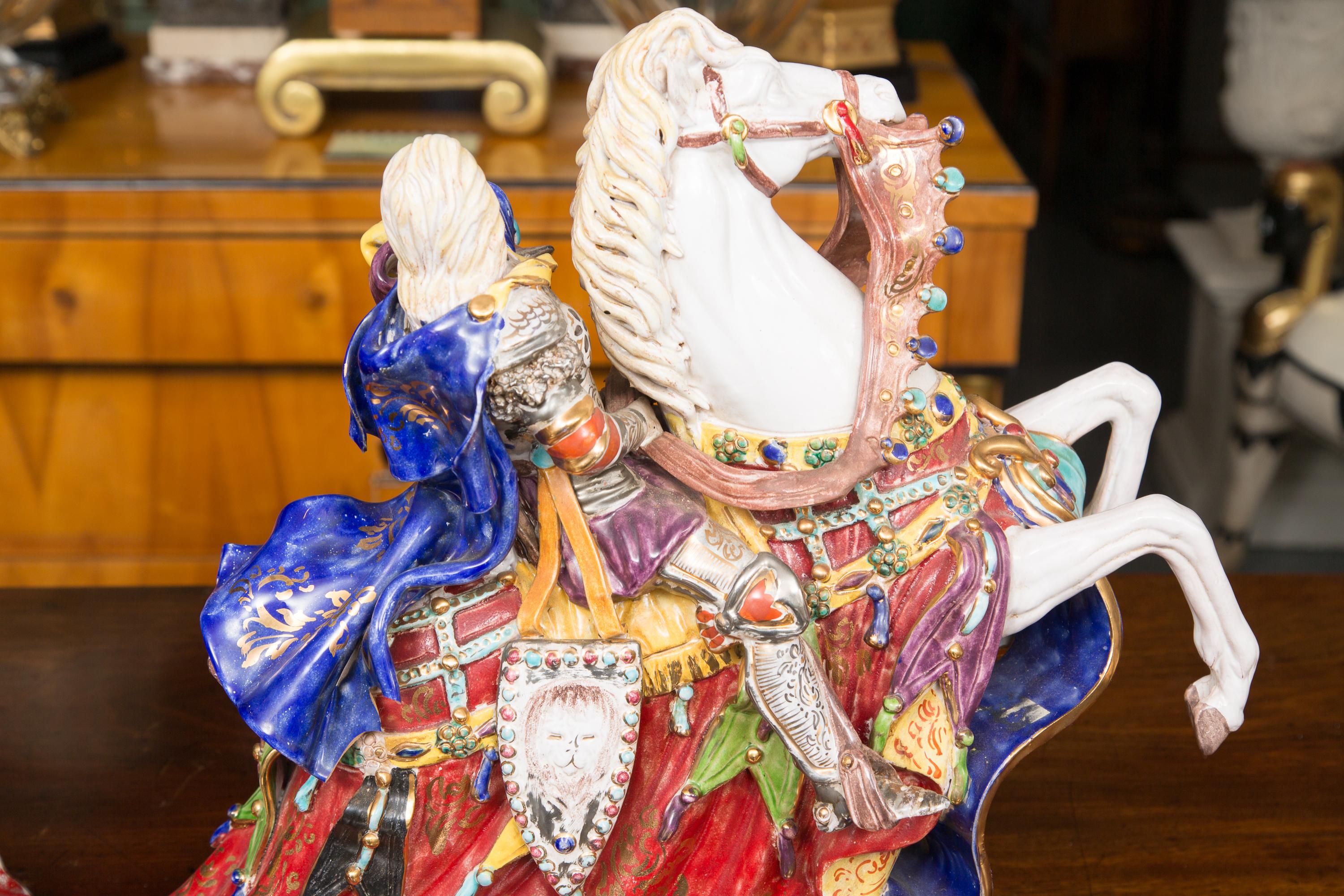 This is a delightful pair of brightly colored Italian glazed porcelain figures depicting elegantly attired knights riding prancing steeds wearing elegant brightly colored saddle draperies. 20th century.