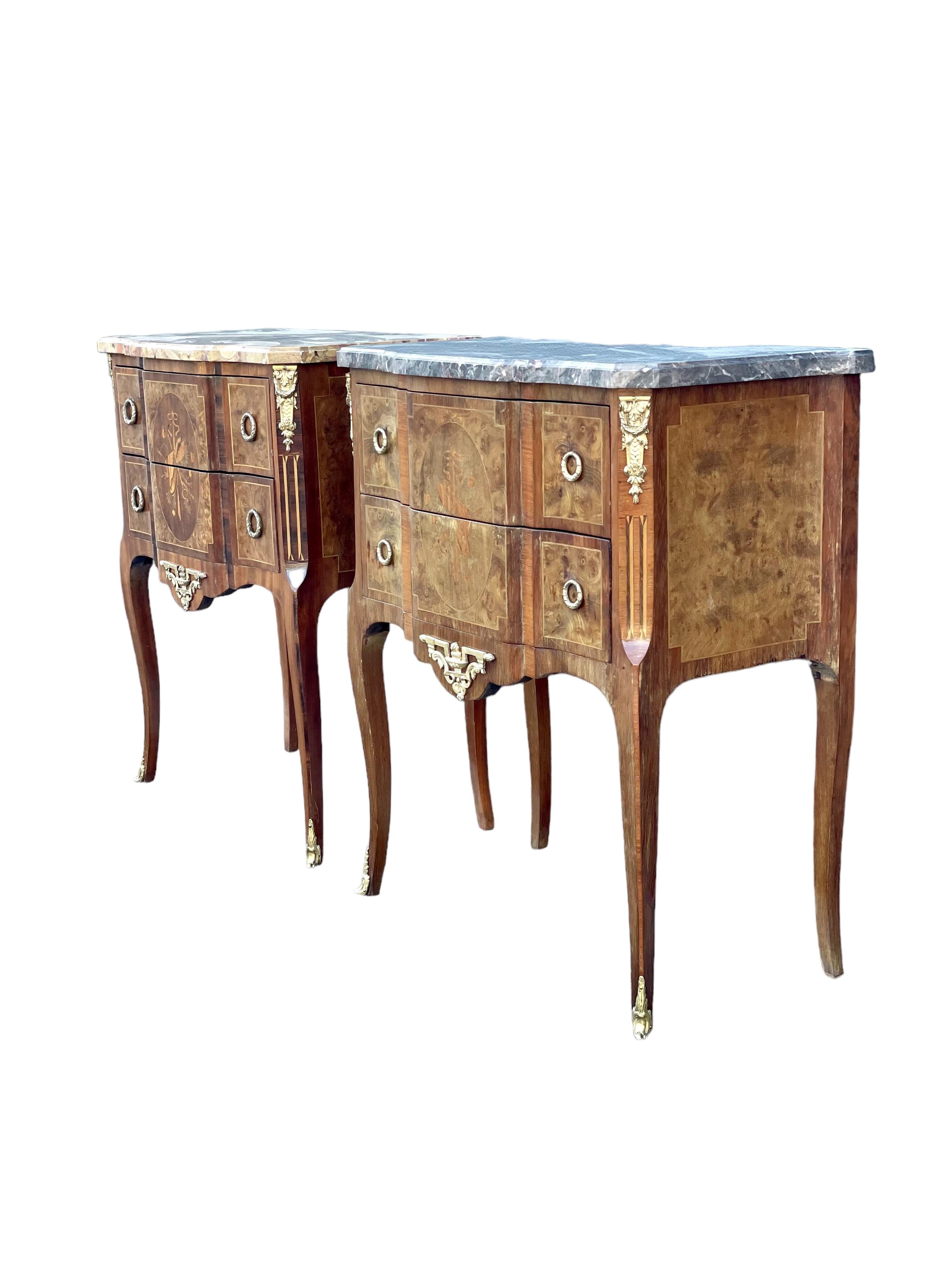 A very stylish and complementary pair of Louis XV/XVI transitional period commodes, each beautifully decorated in veneered wood with inlaid marquetry, and each topped with a contrasting coloured marble top – one grey, and one with yellow-tinted