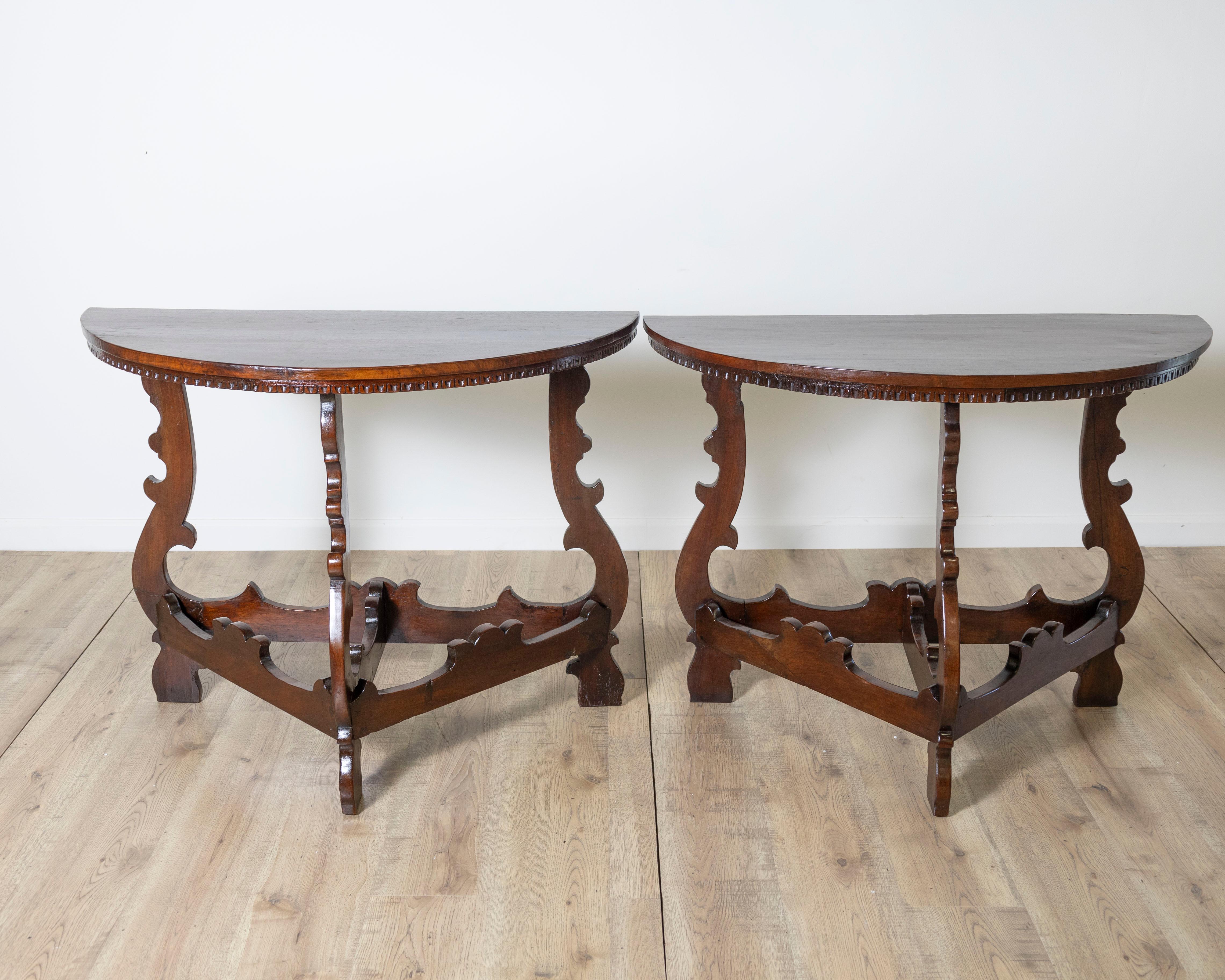 A distinctive pair of 18th-century Italian console tables crafted in solid walnut, showcasing exceptional Baroque influence with bold silhouettes and sculptural forms.

Each console features a demi-lune (half-moon) top with a molded edge, resting on