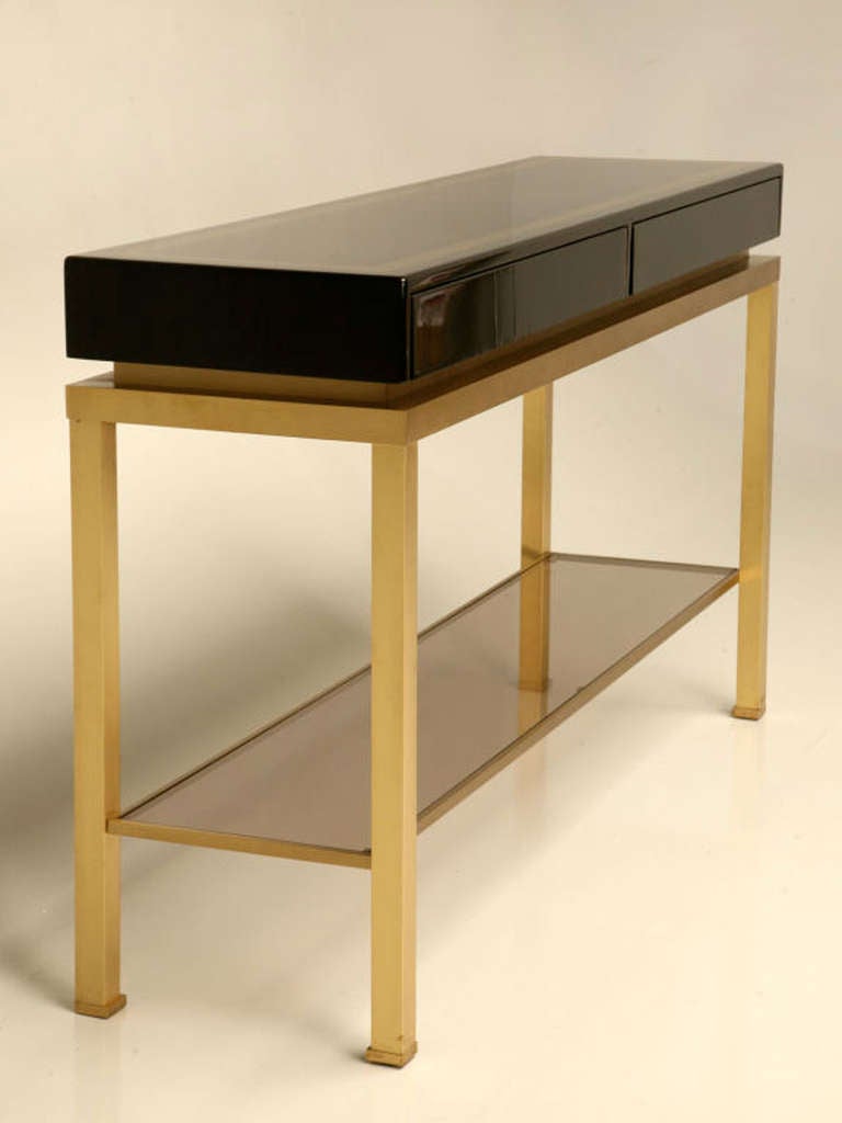 Beautiful pair of large consoles by Guy Lefevre for Maison Jansen, 1970 period. The base is made in brushed brass, the top in black lacquered wood. With two drawers. shelves are in smoked glass, but it's possible to change for clear glass.