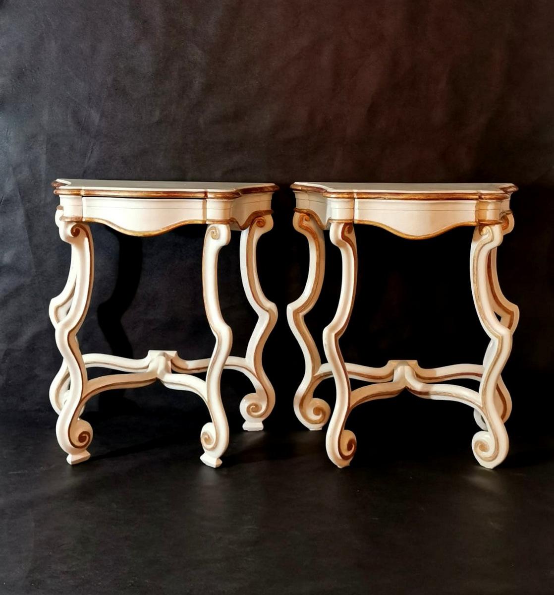  Pair of consoles or bedside tables in white lacquered wood with gold leaf finish; the two pieces of furniture have a graceful and light design, with soft and elegant curves in pure Rococo style; the application of the gold leaf technique along the