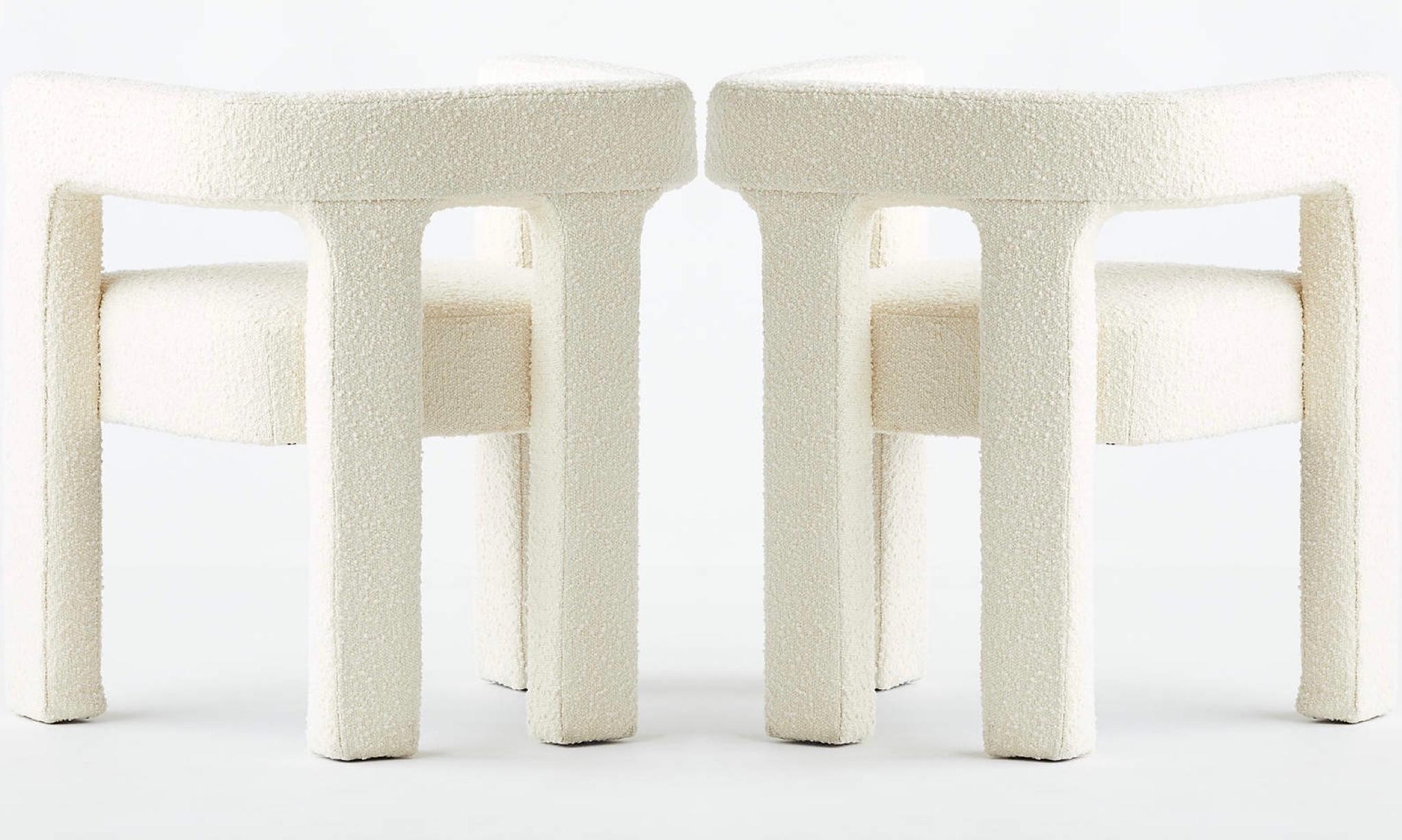 Pair of architectural armchairs in ivory boucle. The mid-century modern style chairs feature sculptural lines with rounded backs and straight legs. Great as lounge chairs, dining room side chairs, or as desk chairs. No leadtime as these are