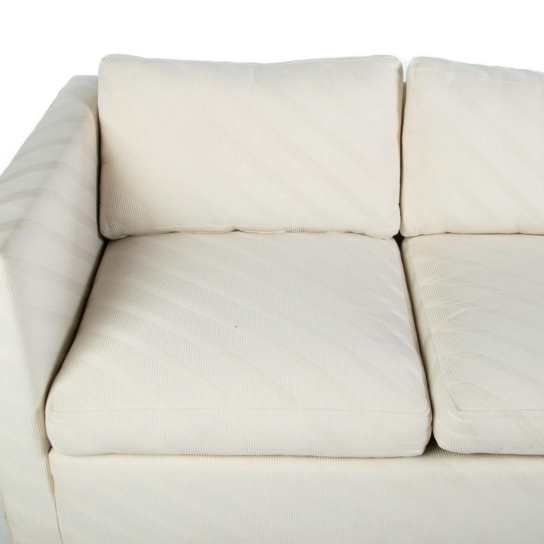 A pair of contemporary three seat sofas in cream tone-on-tone bias stripe fabric. Straight arms and legs with three seat and three back cushions.