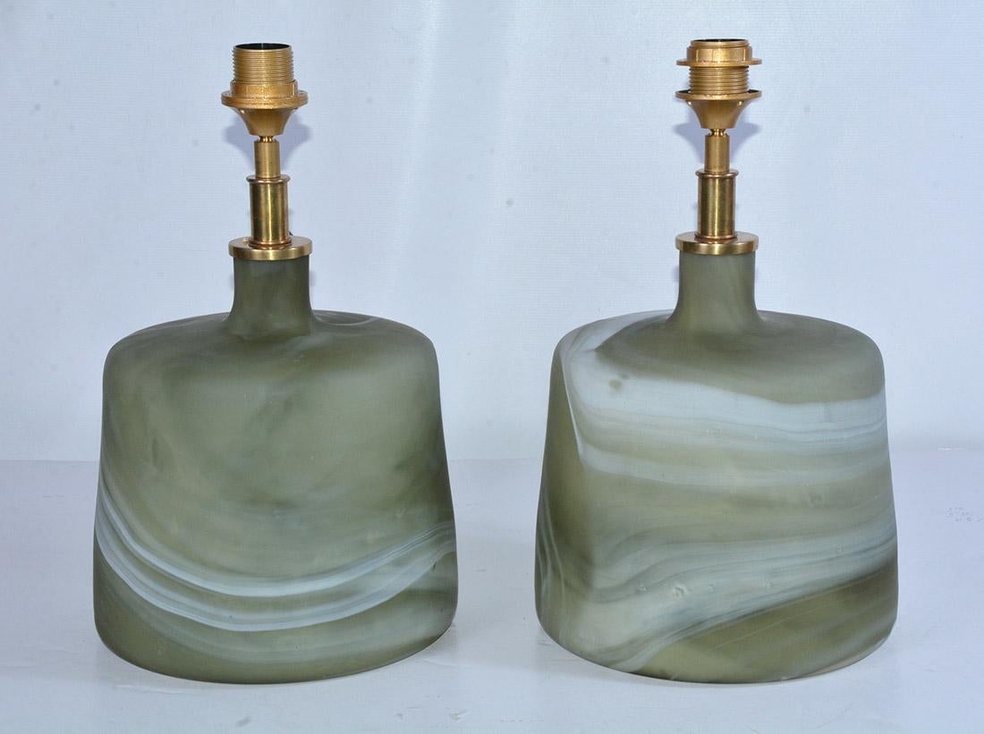 The pair of contemporary one of a kind Murano style green glass lamps have marbleized swirls with mat finish. The designs are not identical. The fixtures are made for European shades. We can change out for you. Cord switch.
