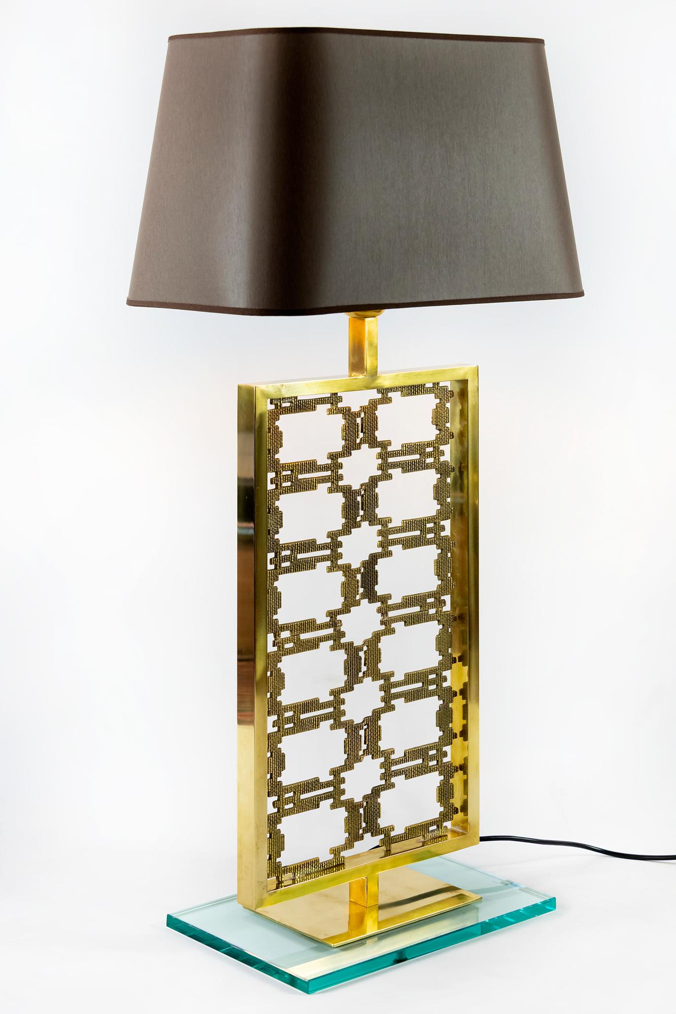 Pair of contemporary Italian table lamps in brass with decorated pattern on it. Solid glass base in transparent color, it measures 24 x 20 cm. Lamps are with E24 bulbs. The shades are new made in satin finish dark brown textile with gold color