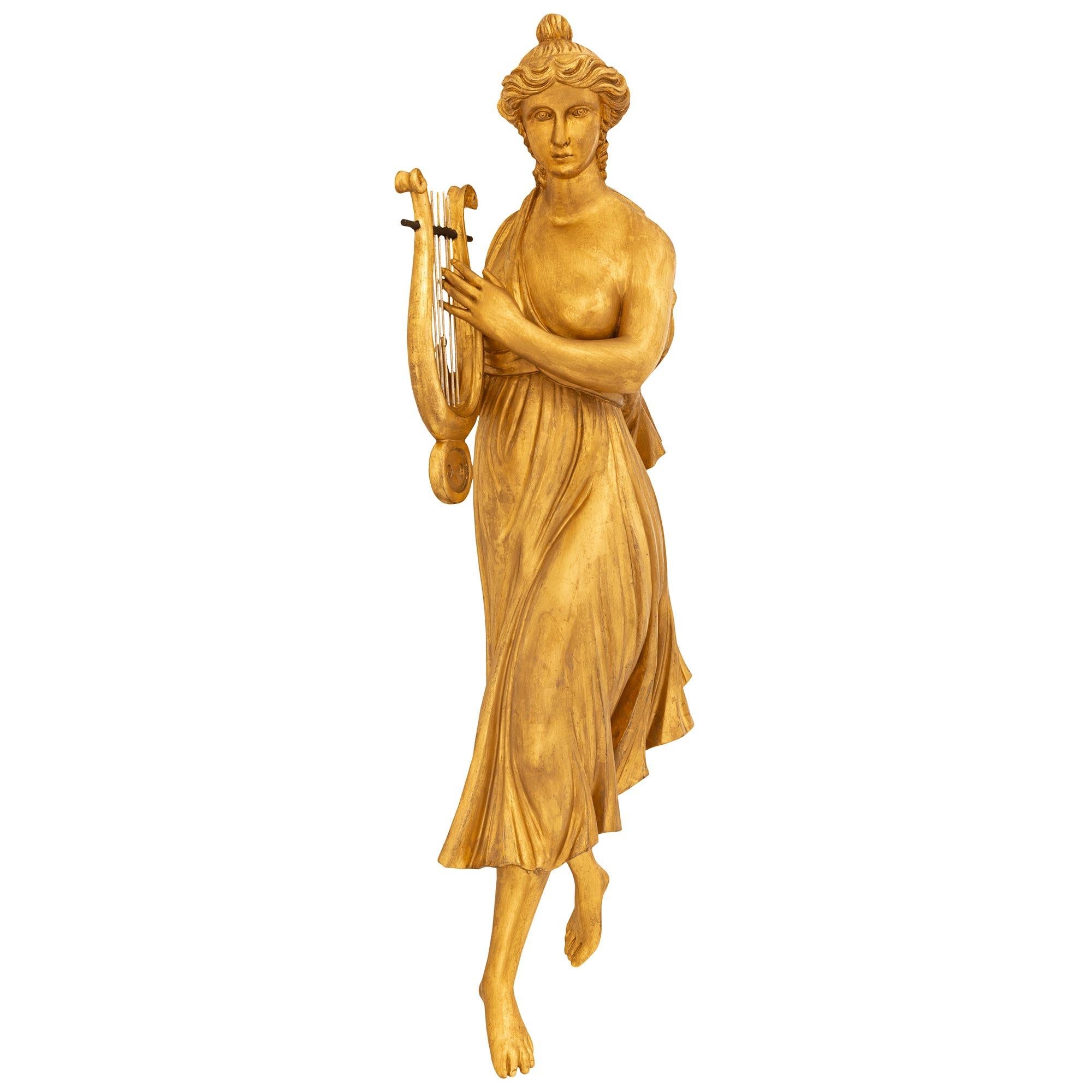 Paire de décorations murales en bois doré de style Louis XVI du XIXe siècle. Chacune des jeunes filles richement sculptées porte une tenue classique, les cheveux relevés, et tient son instrument de musique à deux mains. La jeune fille de gauche