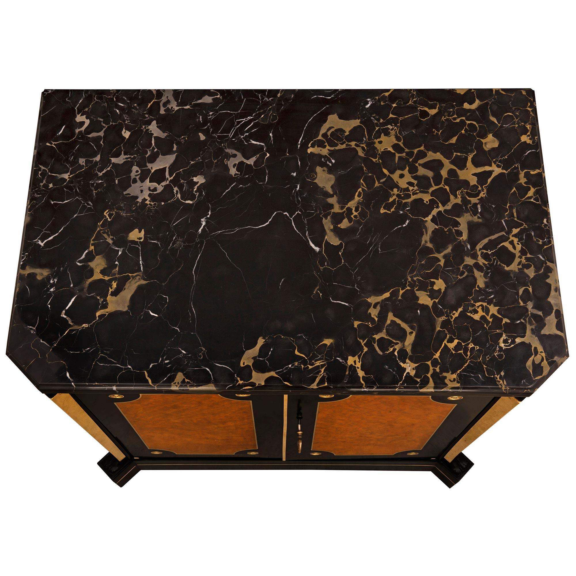 A handsome and most unique pair of Continental 19th century Neo-Classical st. ebony, ash wood, ormolu and Portoro marble cabinets. Each cabinet is raised by a straight base with elegant cut corners. Leading up each side are impressive decorative