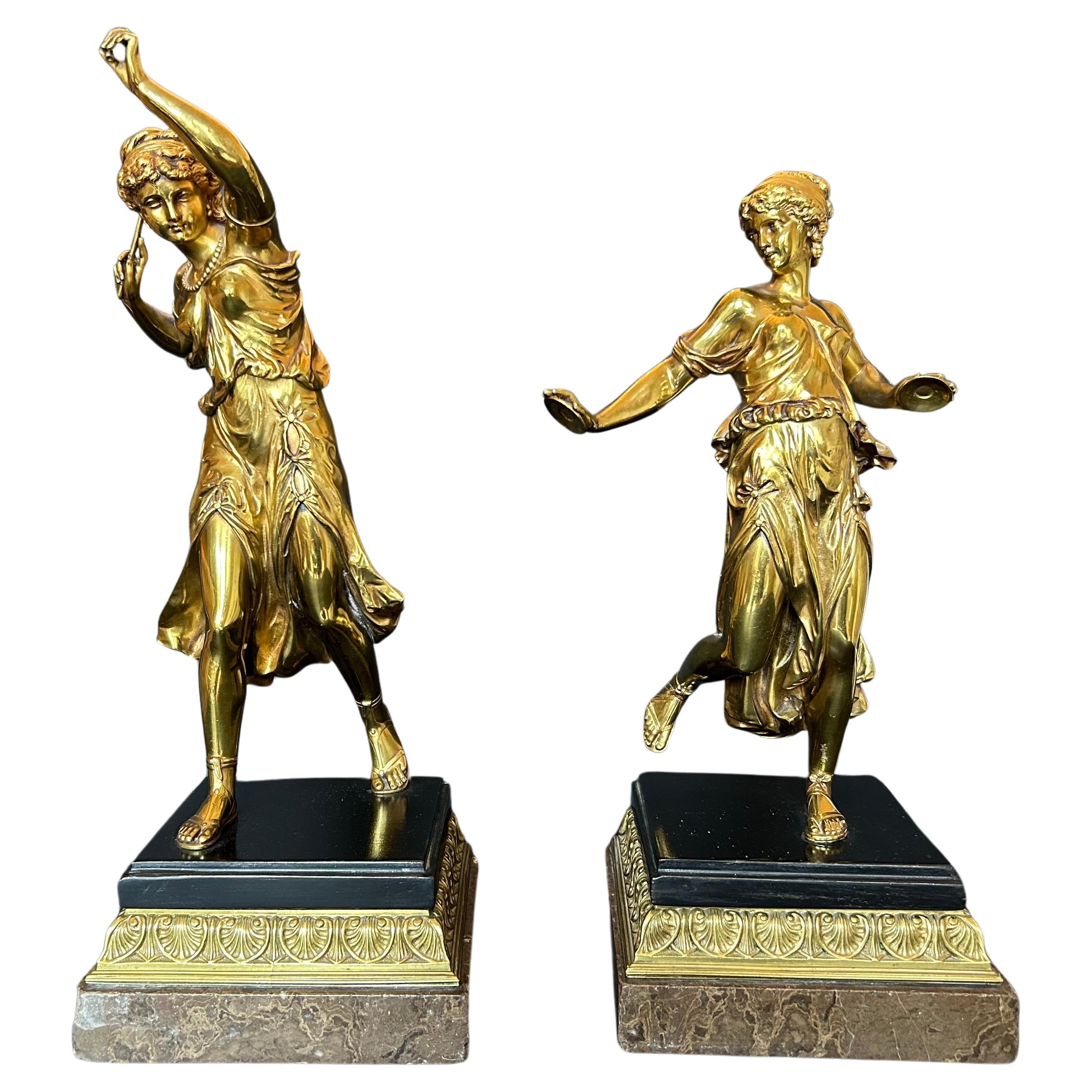 Magnifique paire de sculptures en bronze doré représentant deux danseurs dans le style grec classique, l'un tenant des cymbales et l'autre un bâton. Chacune repose sur une base en marbre à étages avec des détails en acanthe et en bronze doré. Début