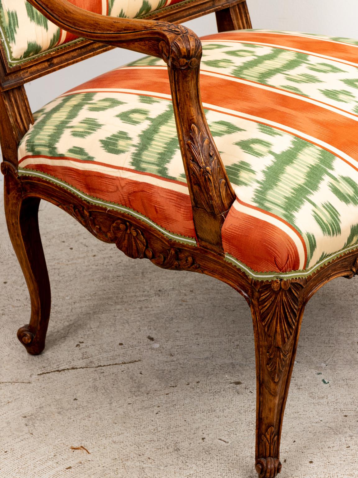 Pair of upholstered Continental style open armchairs on cabriole legs with carved scrolled foliage as seen on the seat apron. Please note of wear consistent with age including finish loss and minor chips.