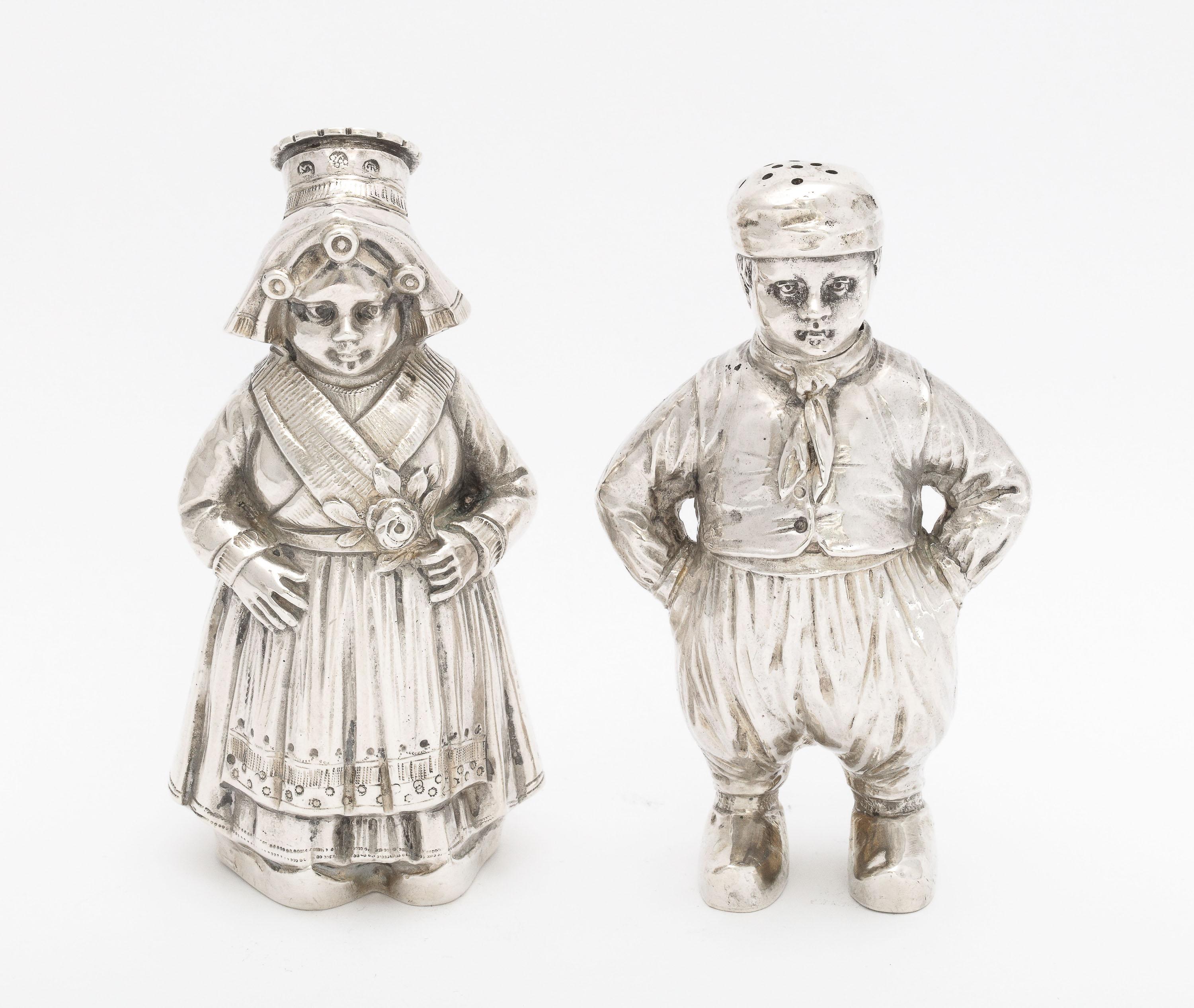 Pair of Edwardian Period, Continental Silver (.835) salt and pepper shakers in the form of a Dutch Girl and Boy, Austria, Ca. 1900. The removable, pierced hat of each shaker serves as the lid of that shaker. The closure is a bayonet closure. The