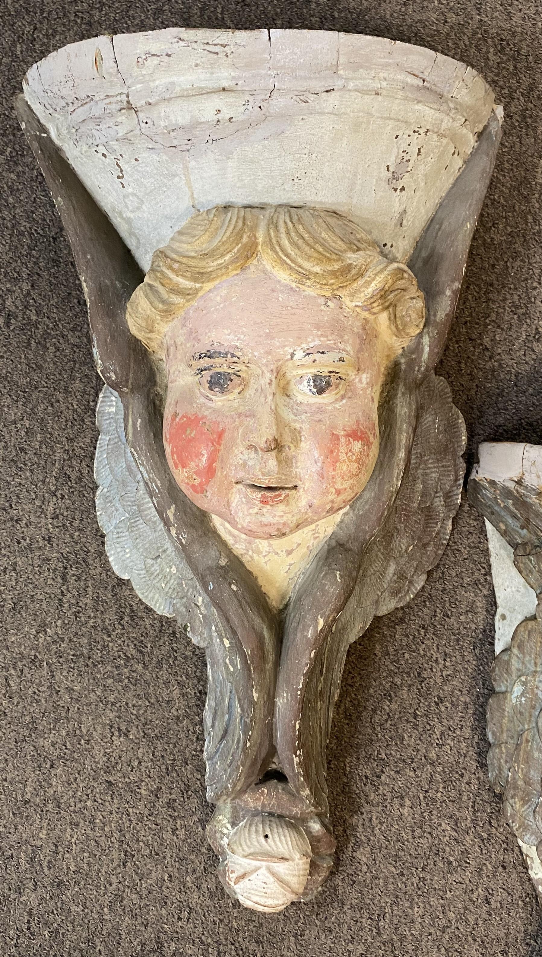 A fine pair of Continental wooden polychrome figural wall appliqués or brackets with cherub faces adorned with side wings, each hand carved from a single piece of wood, probably dating to the 19th century. Very good overall condition, with some edge