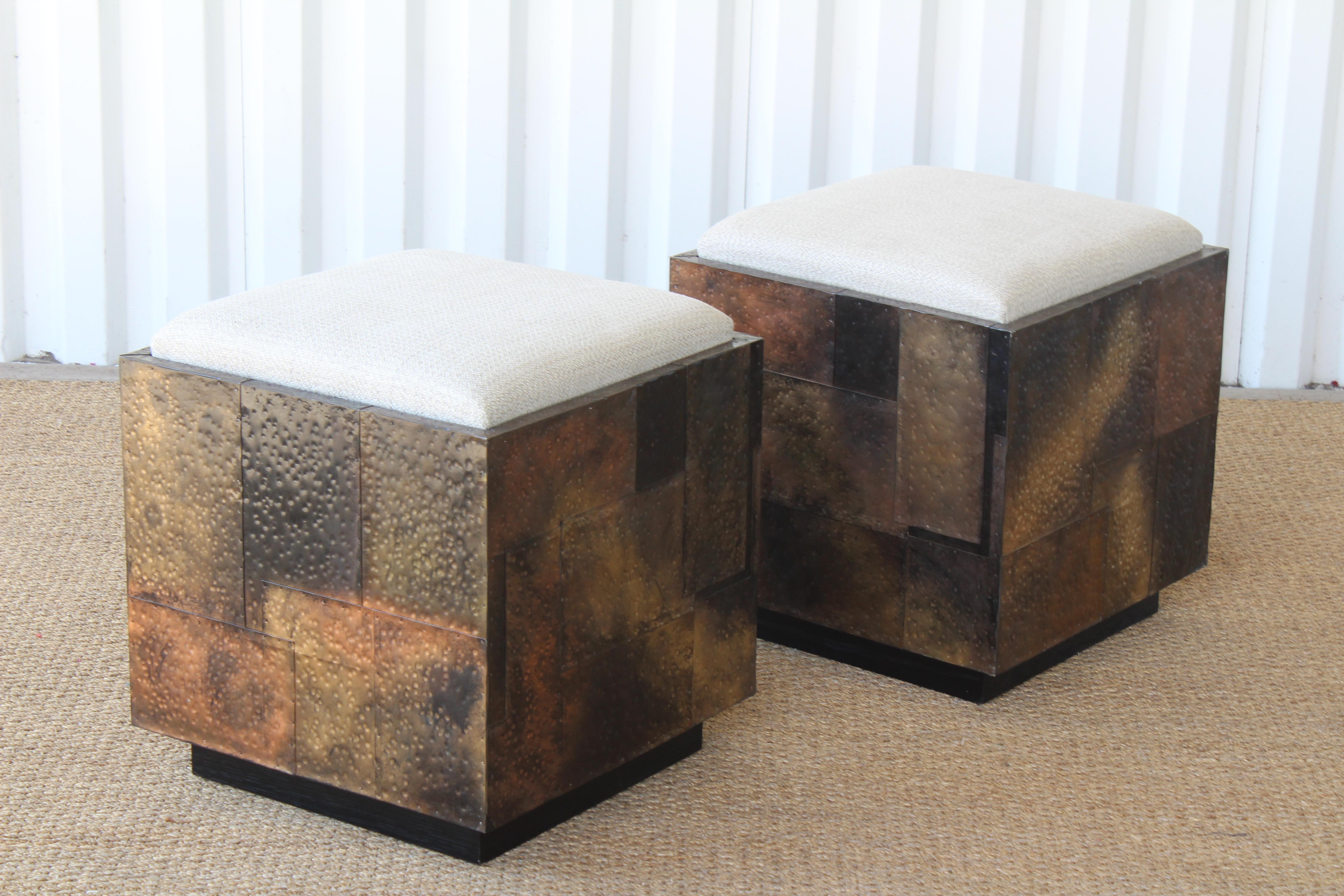 Pair of copper-clad stools or ottomans in the style of Paul Evans. Each stool rolls on casters and features removable seats for additional hidden storage. Seats are upholstered in a neutral linen. Sit on walnut plinth bases with new black finish. In