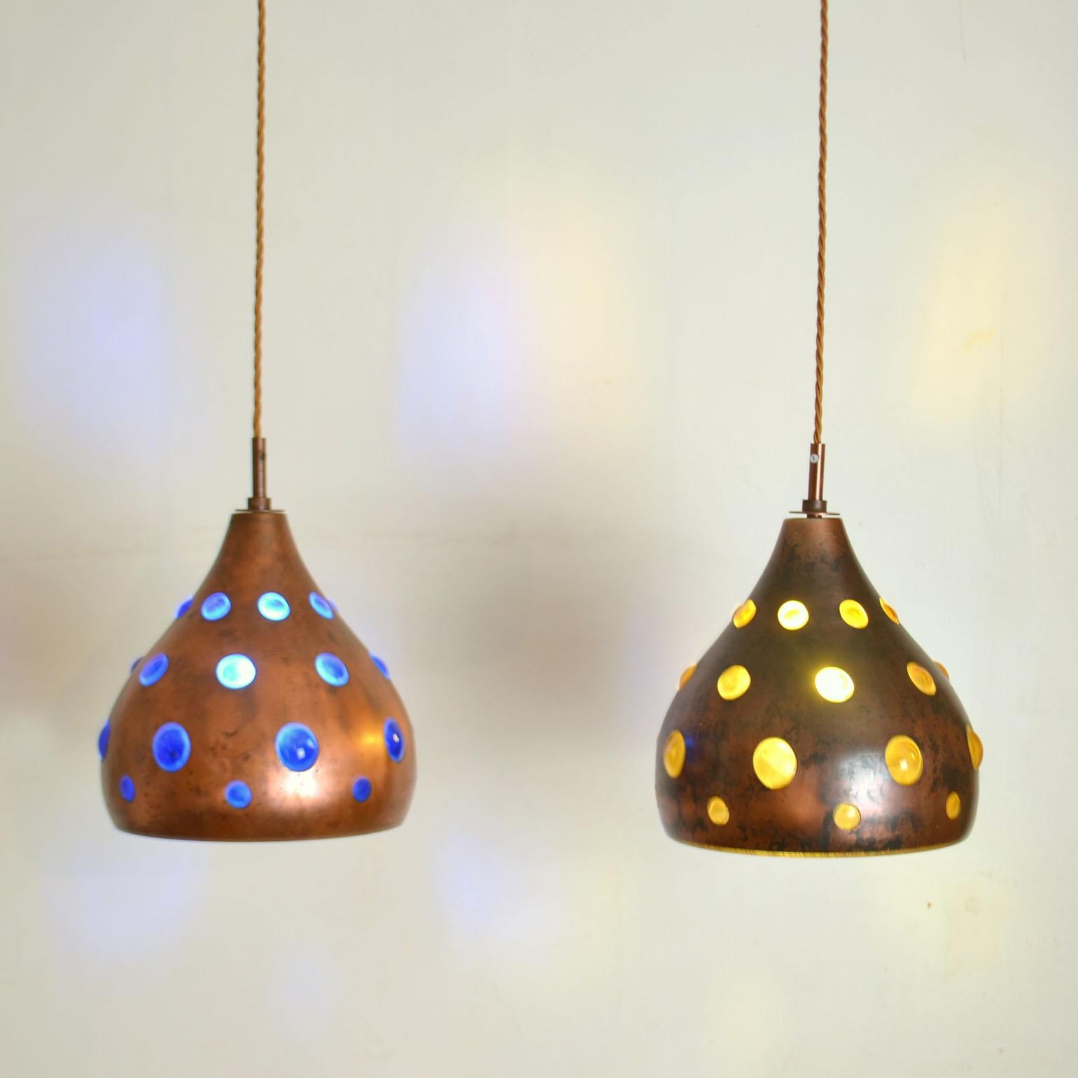 Pair of blue and amber pendant lamps are made from blown glass & oxidized copper. They are all unique in execution. The deep blue and amber expanded glass is blown with regularity into external patinated copper spherical or rectangular frames. The