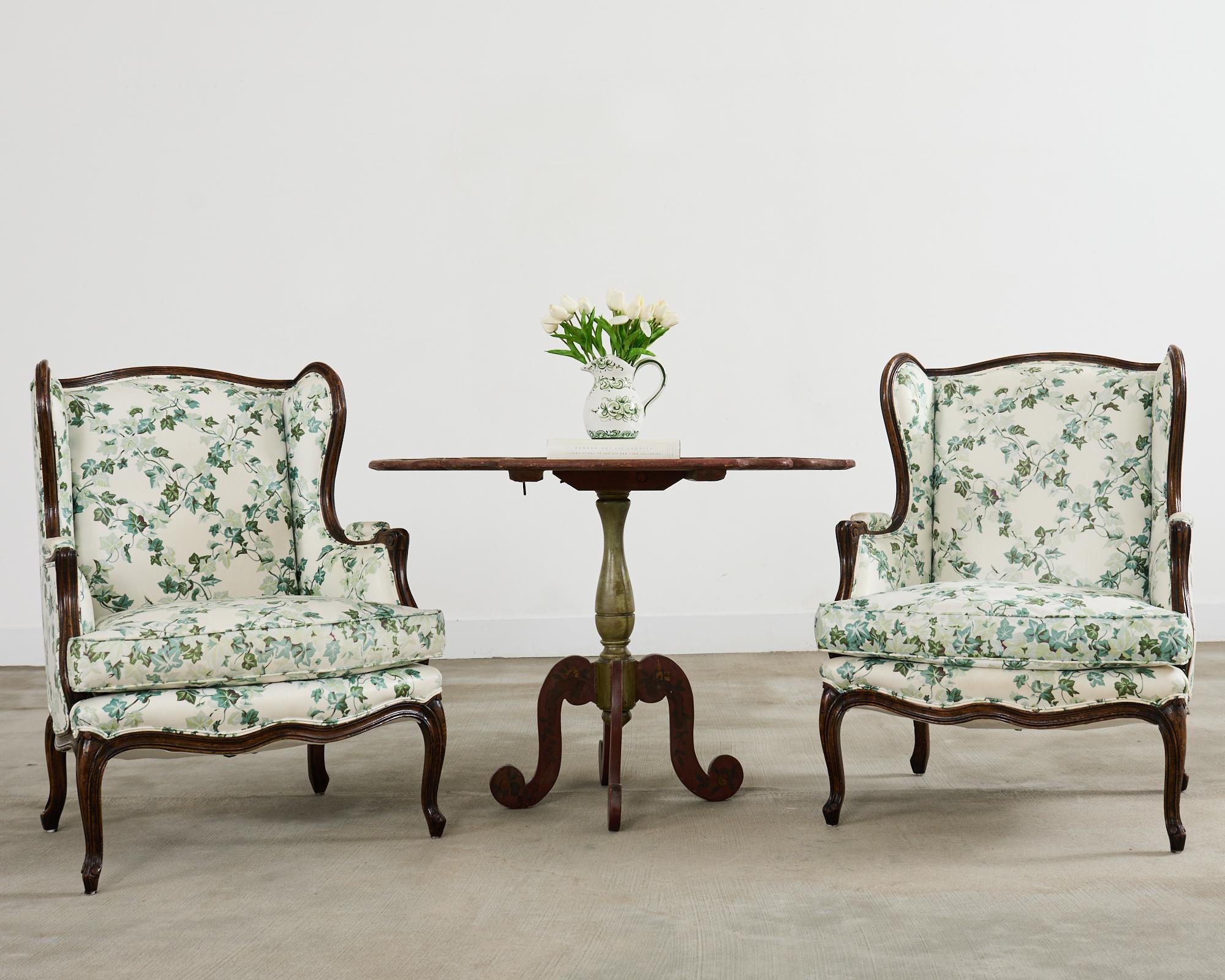 Amazing pair of country French provincial or Louis XV style wingback armchairs crafted from walnut. The chairs are constructed from walnut with gracefully curved large wings and a generous seat. The chairs have been restored and reupholstered in the